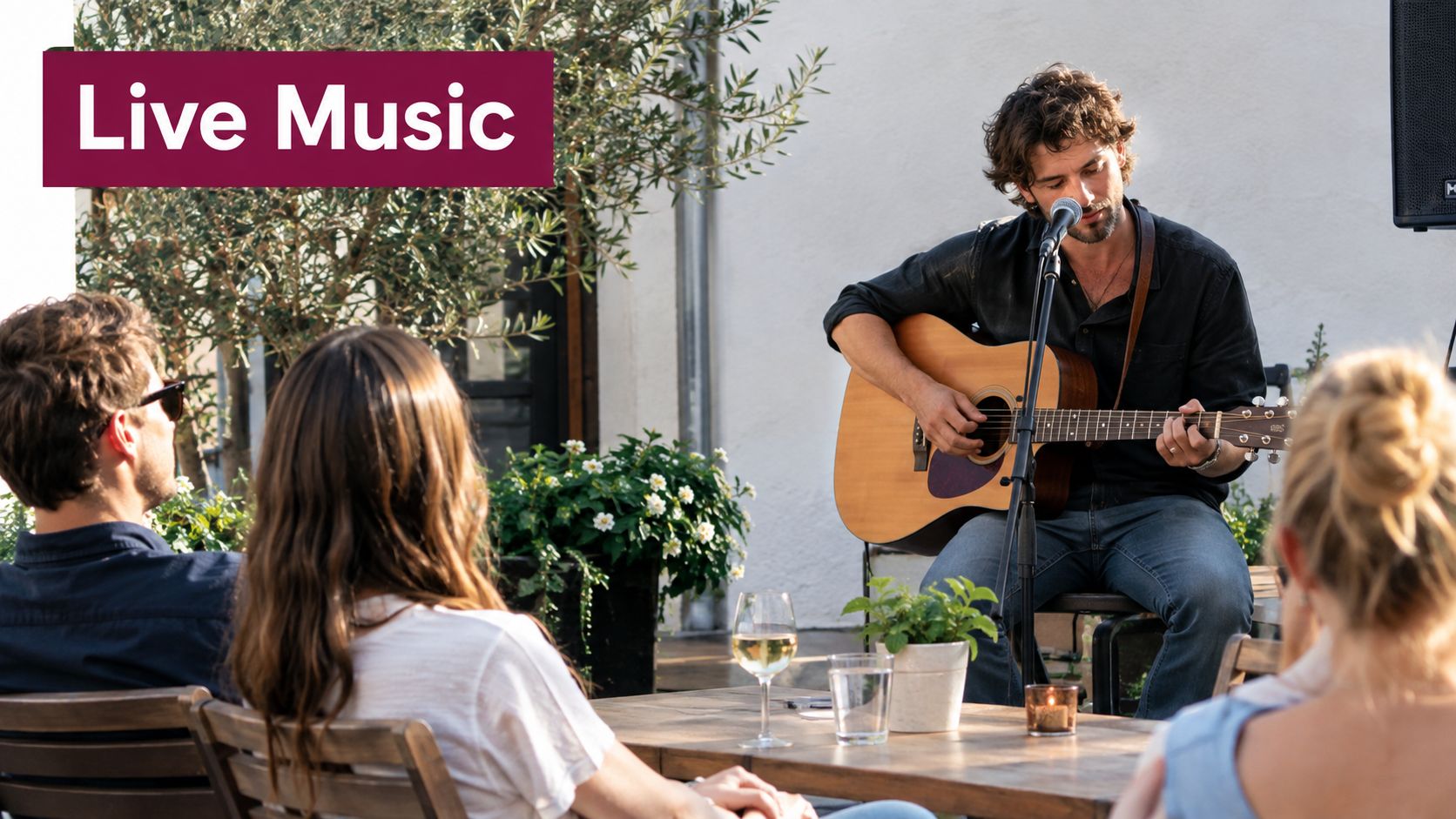 A musician plays acoustic guitar and sings for people sitting at an outdoor restaurant table.
