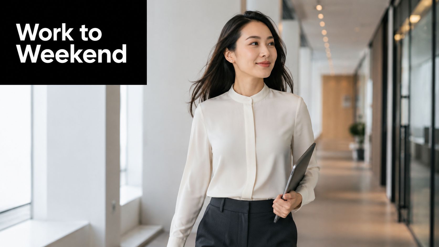 A professional Asian woman in a mandarin collar blouse walking down a bright modern office hallway.