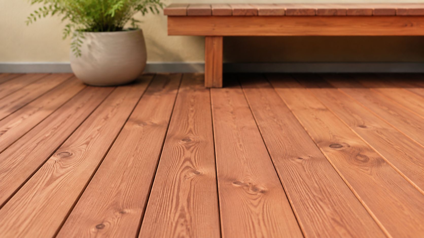 Close-up of natural wooden decking boards with a potted plant and bench on a balcony patio.