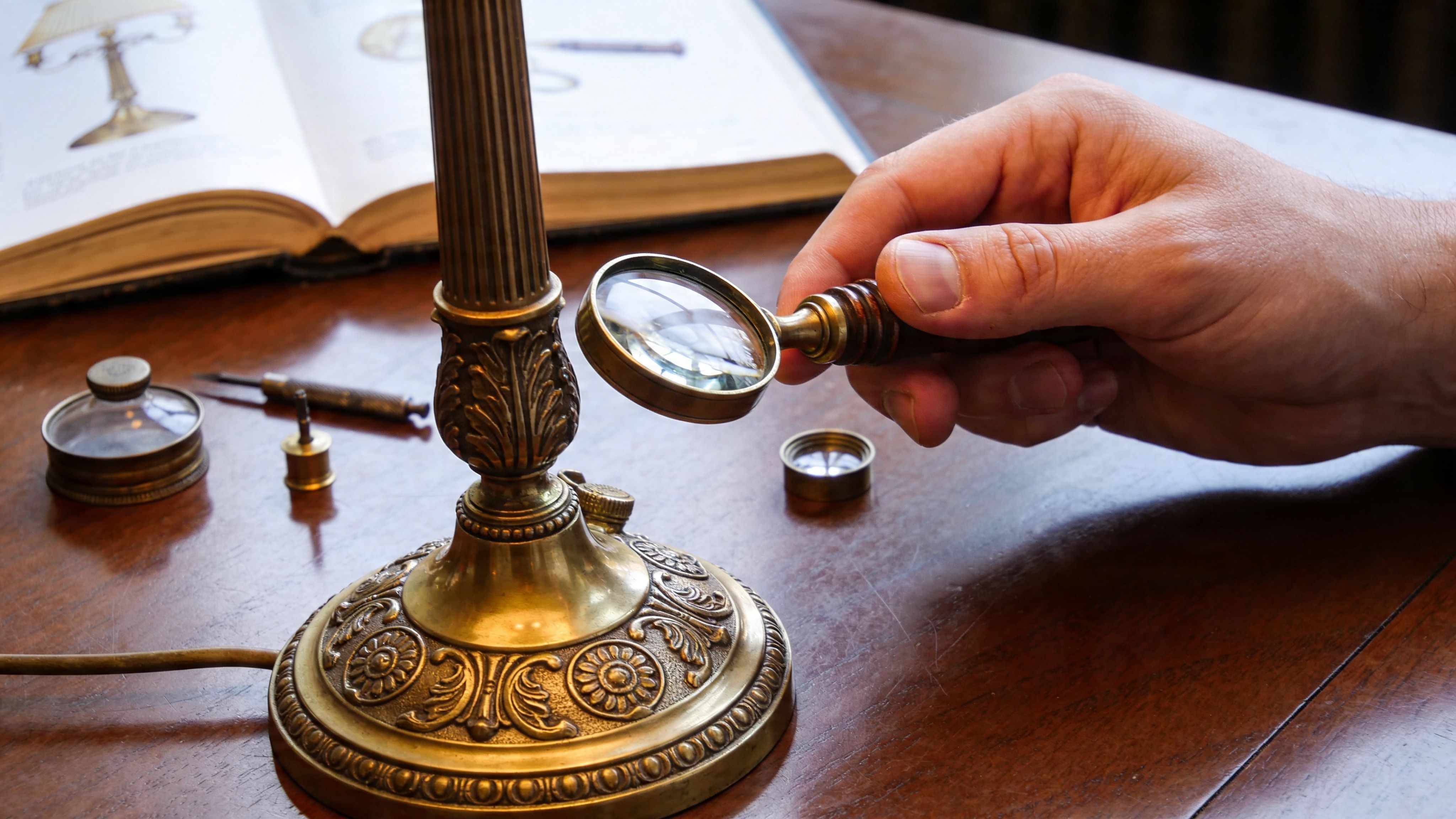 A close-up of a person examining the base of an ornate vintage table lamp with a magnifying glass.