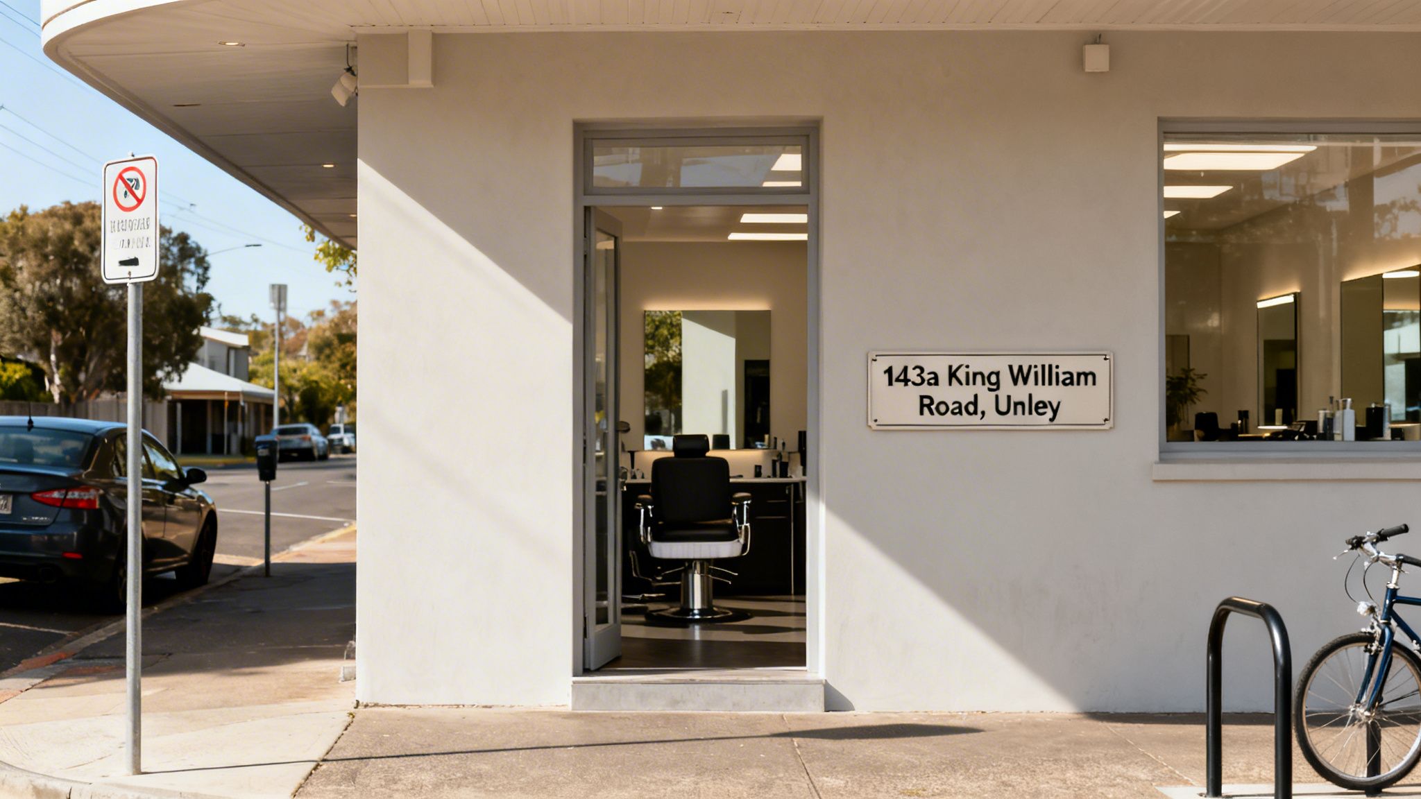 Exterior view of a bright barber shop with an open door, an address sign, and a street scene.