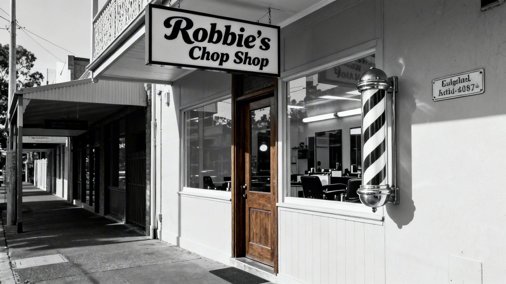 Black and white photo of Robbie's Chop Shop exterior, featuring a barber pole and a long street view.