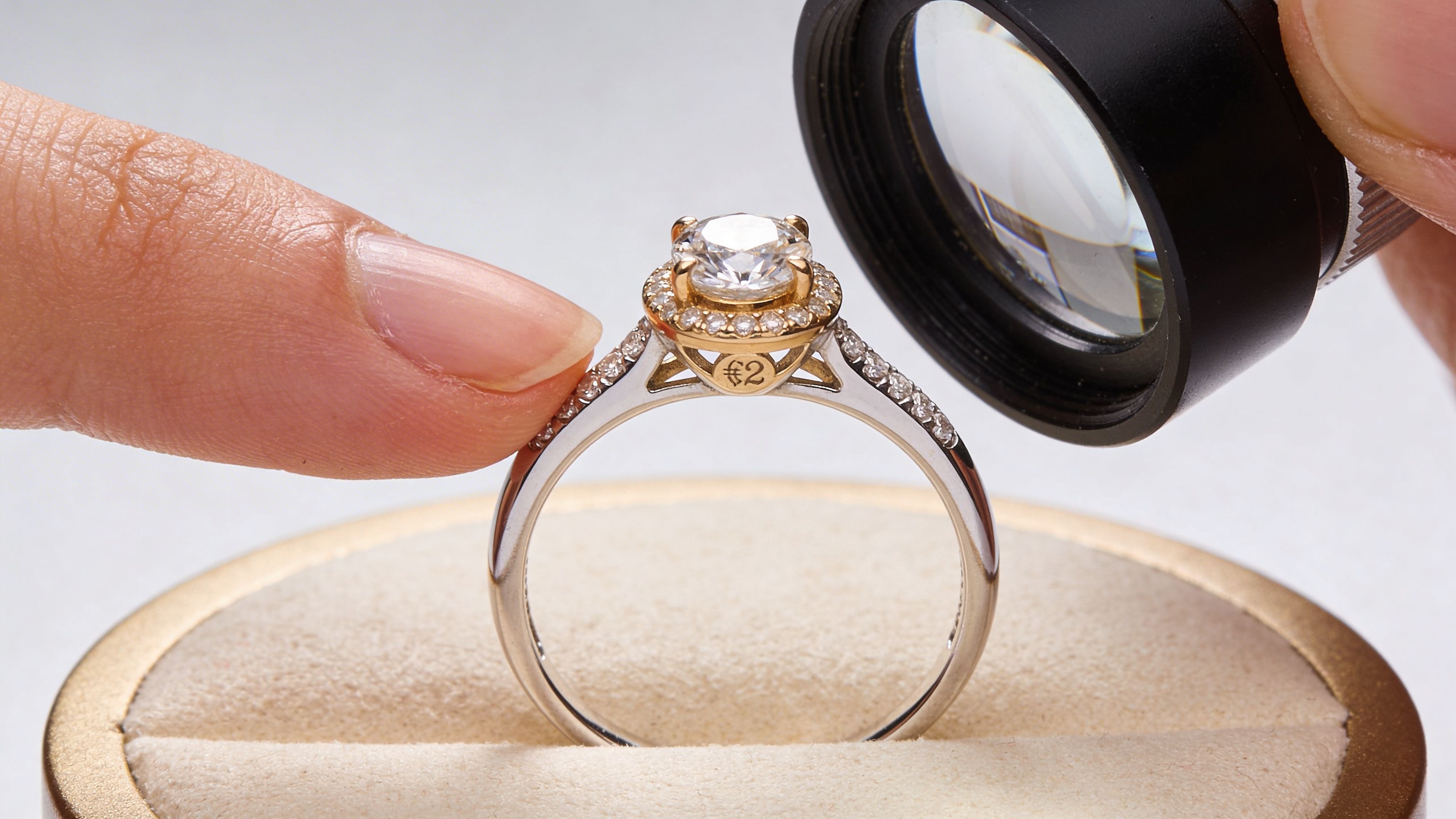 A close-up view of a diamond ring being inspected with a magnifying glass held by a person.