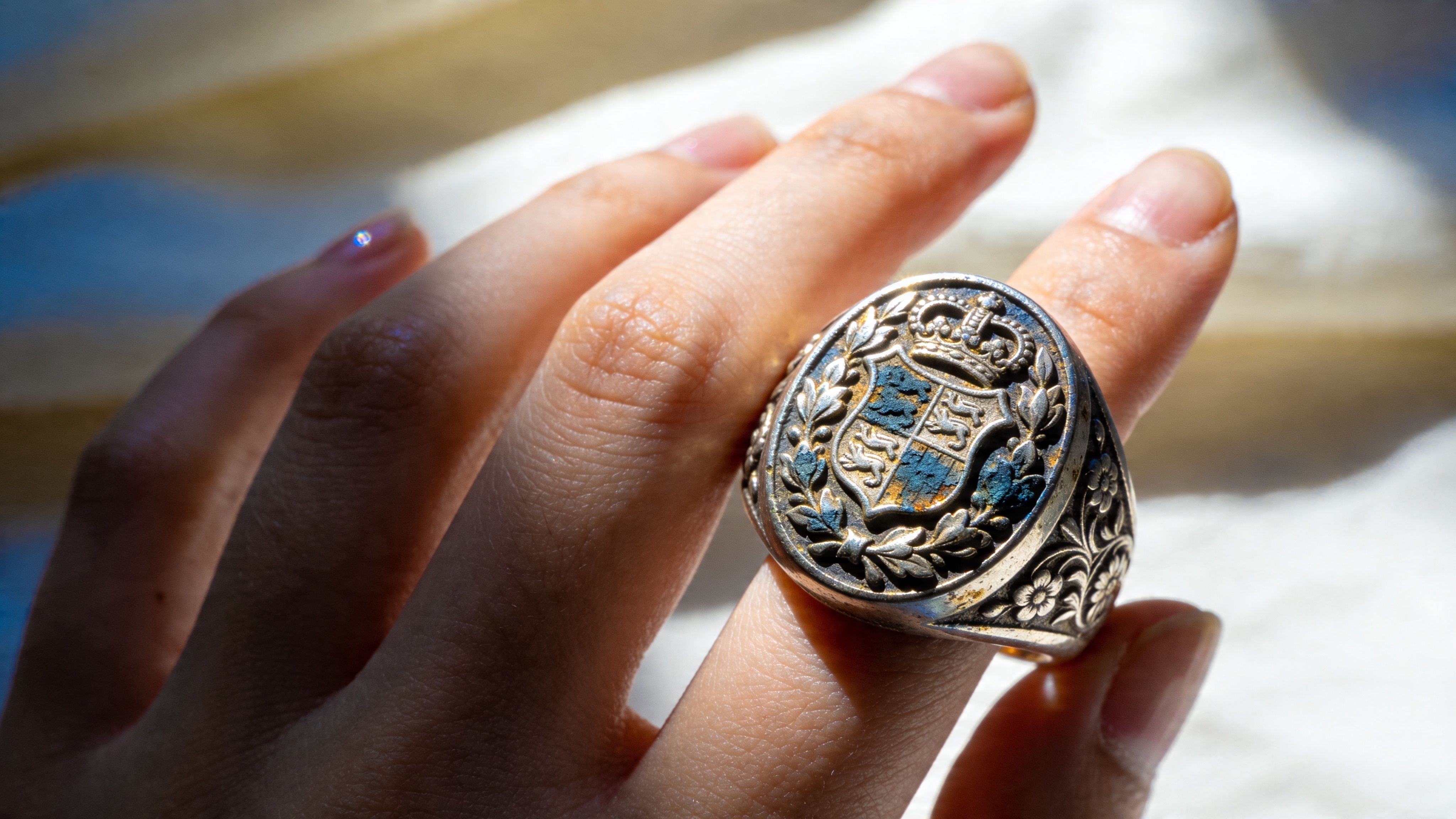 A close-up view of an intricate silver crest ring being held on a finger.