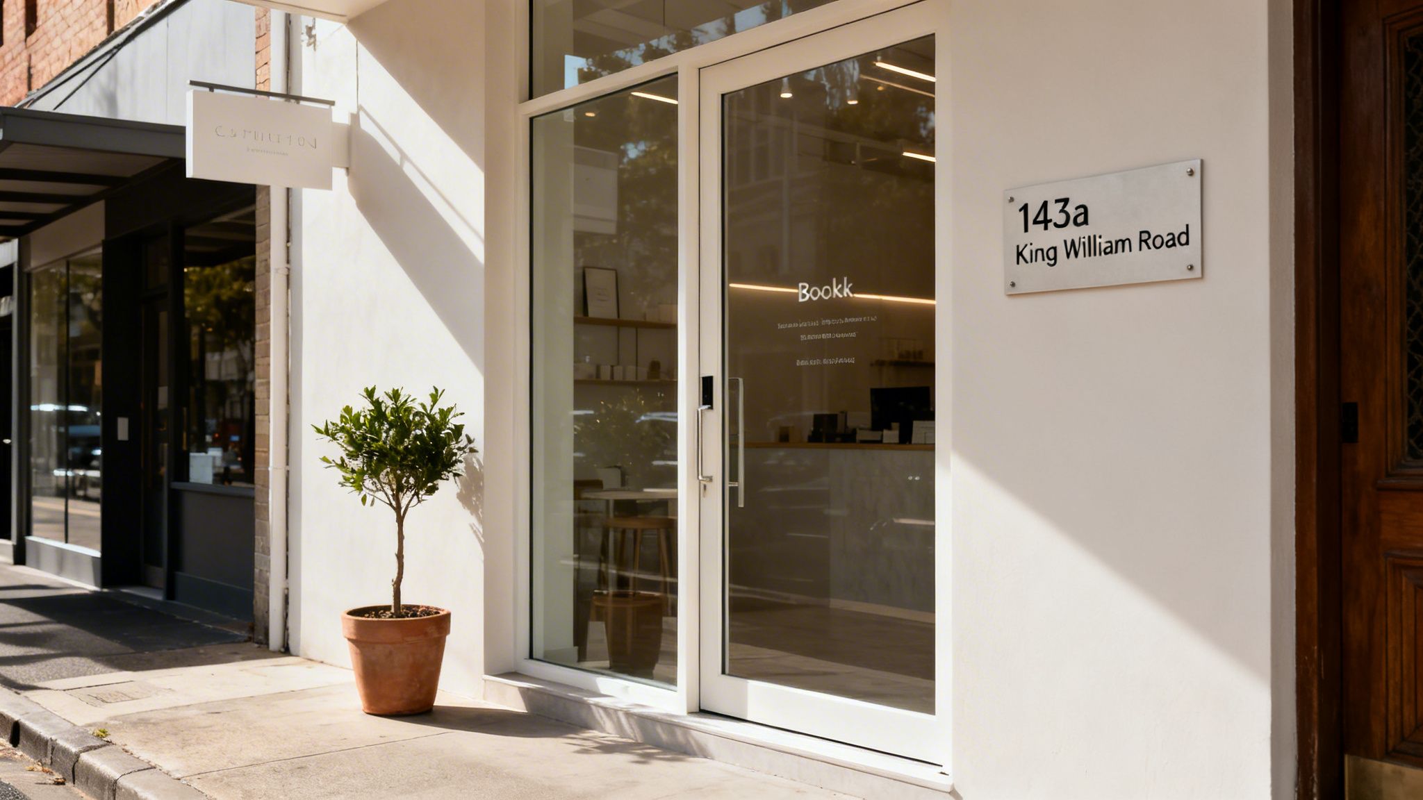 Exterior view of a modern storefront named Bookk, featuring a potted plant and address 143a King William Road.