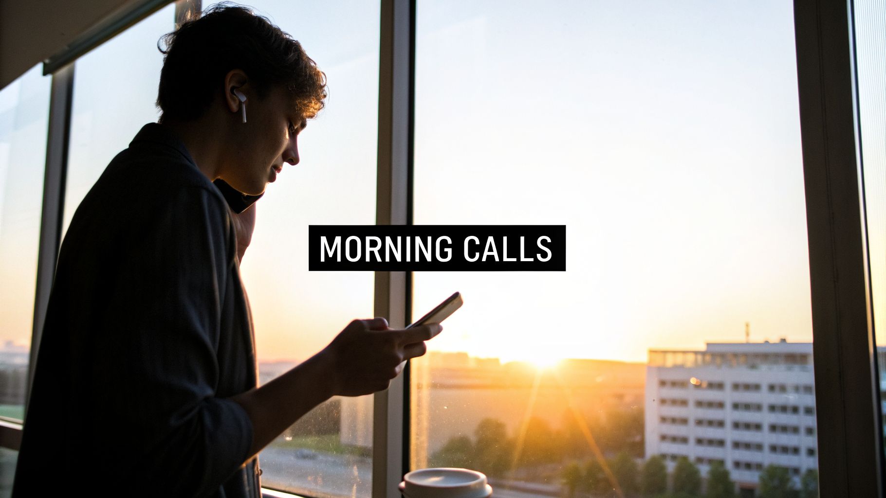 A young person with AirPods looks at their phone by a window with a bright morning sunrise.