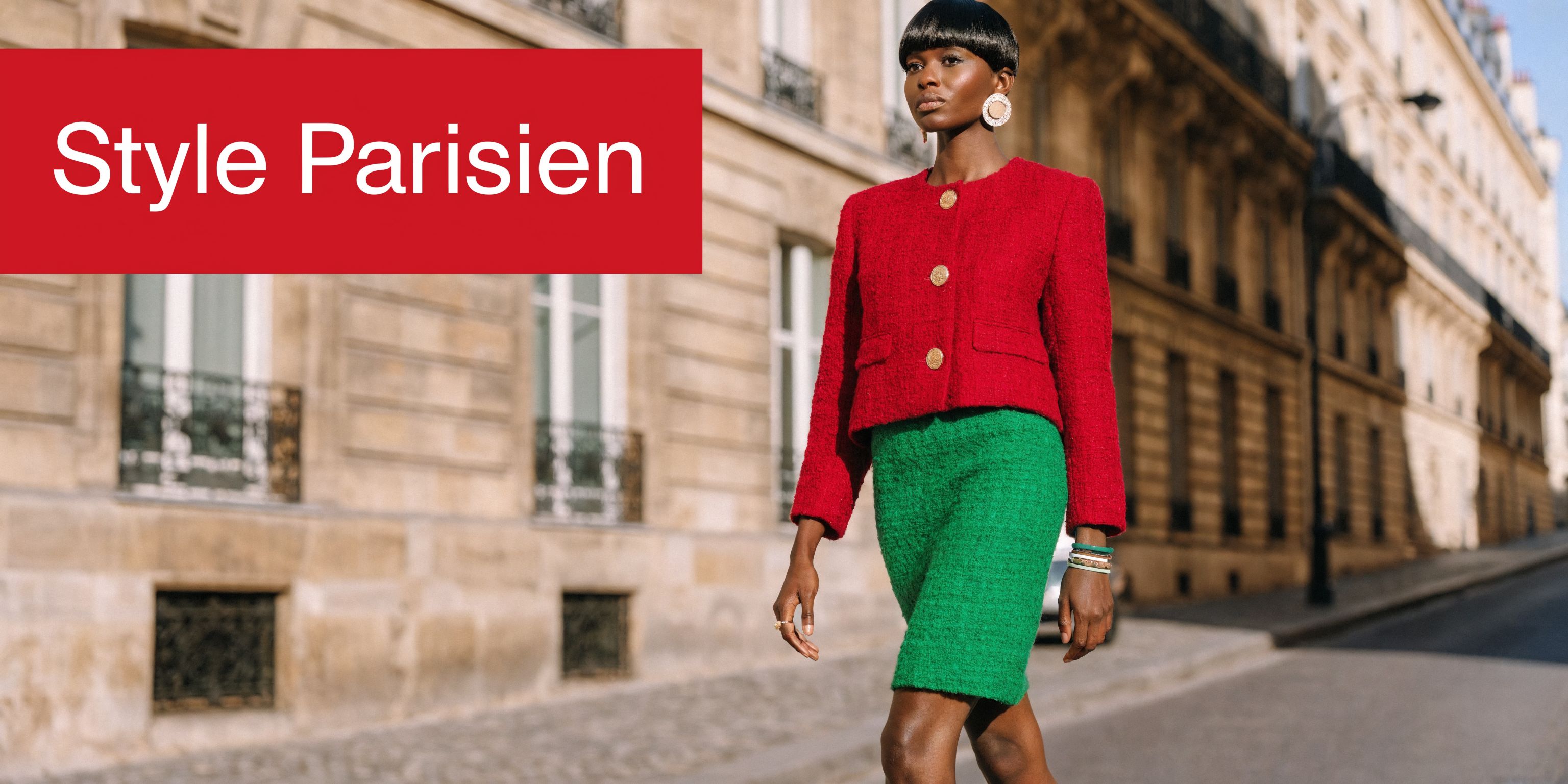 Une femme noire élégante avec une coupe pixie porte une veste rouge et une jupe verte à Paris.