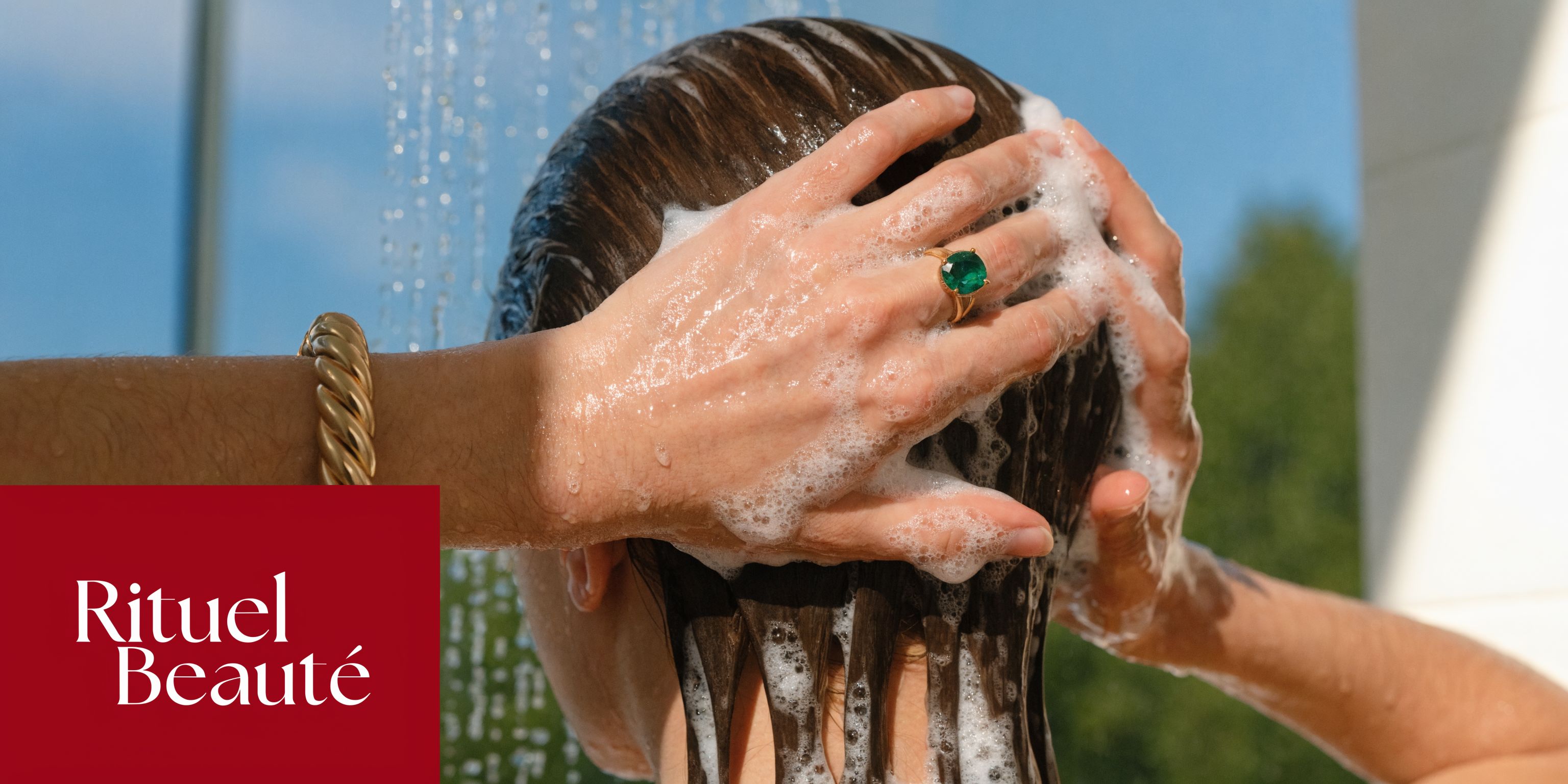 Une personne se lave les cheveux sous la douche avec du shampoing tout en portant des bijoux dorés.