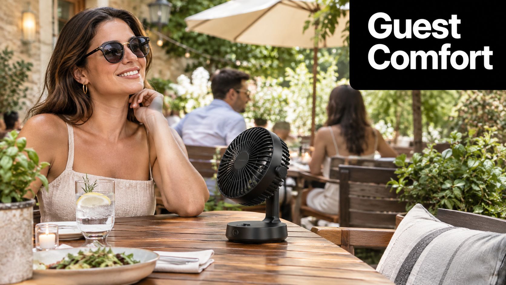 A woman smiling at an outdoor restaurant table with a compact black battery operated fan nearby.