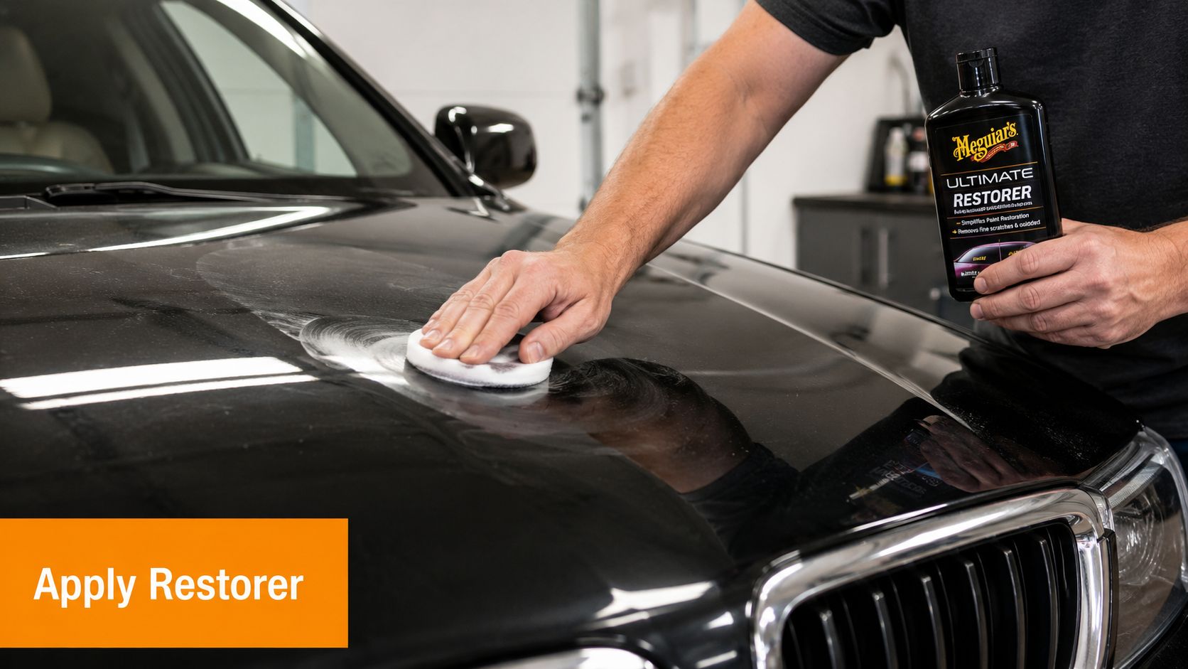 A person applying Meguiar's Ultimate Restorer to a black car hood using a white foam applicator pad.