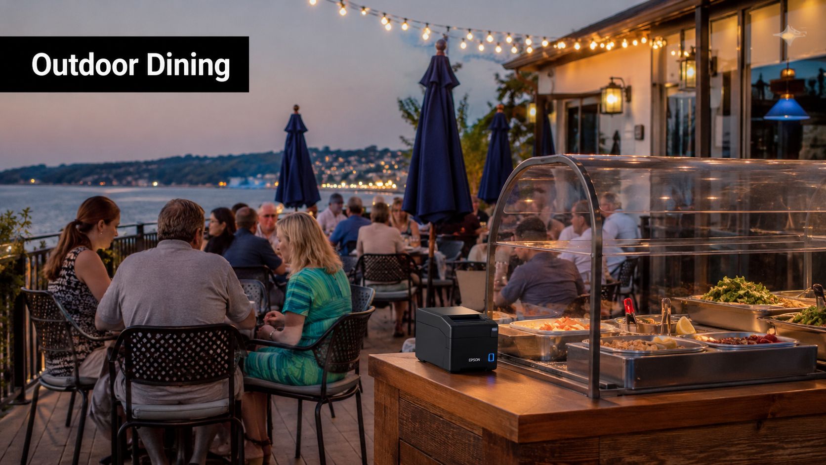 Patrons enjoy an outdoor seaside dining experience at a restaurant with buffet food stations at sunset.