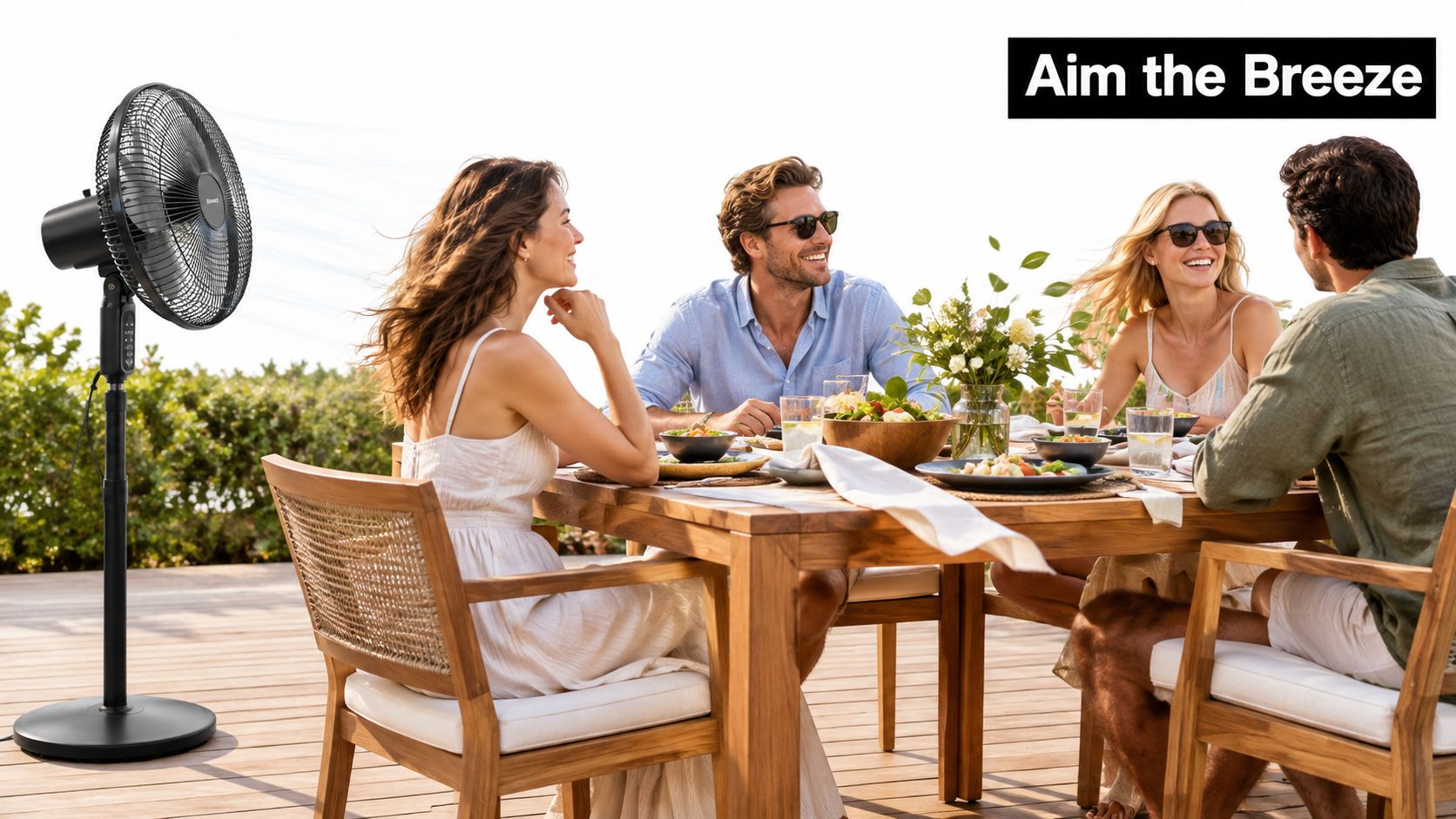 A modern outdoor stand fan providing a gentle breeze for friends dining at a wooden patio table.