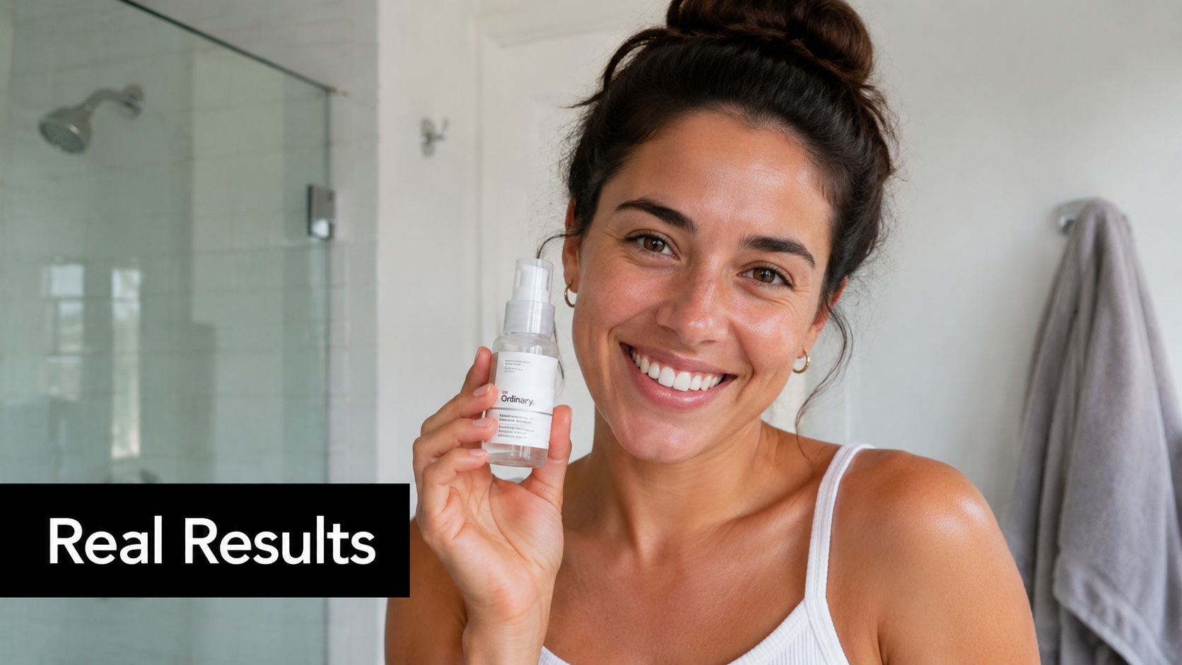 A smiling woman holding The Ordinary skincare product in a bathroom, showcasing glowing and healthy skin.