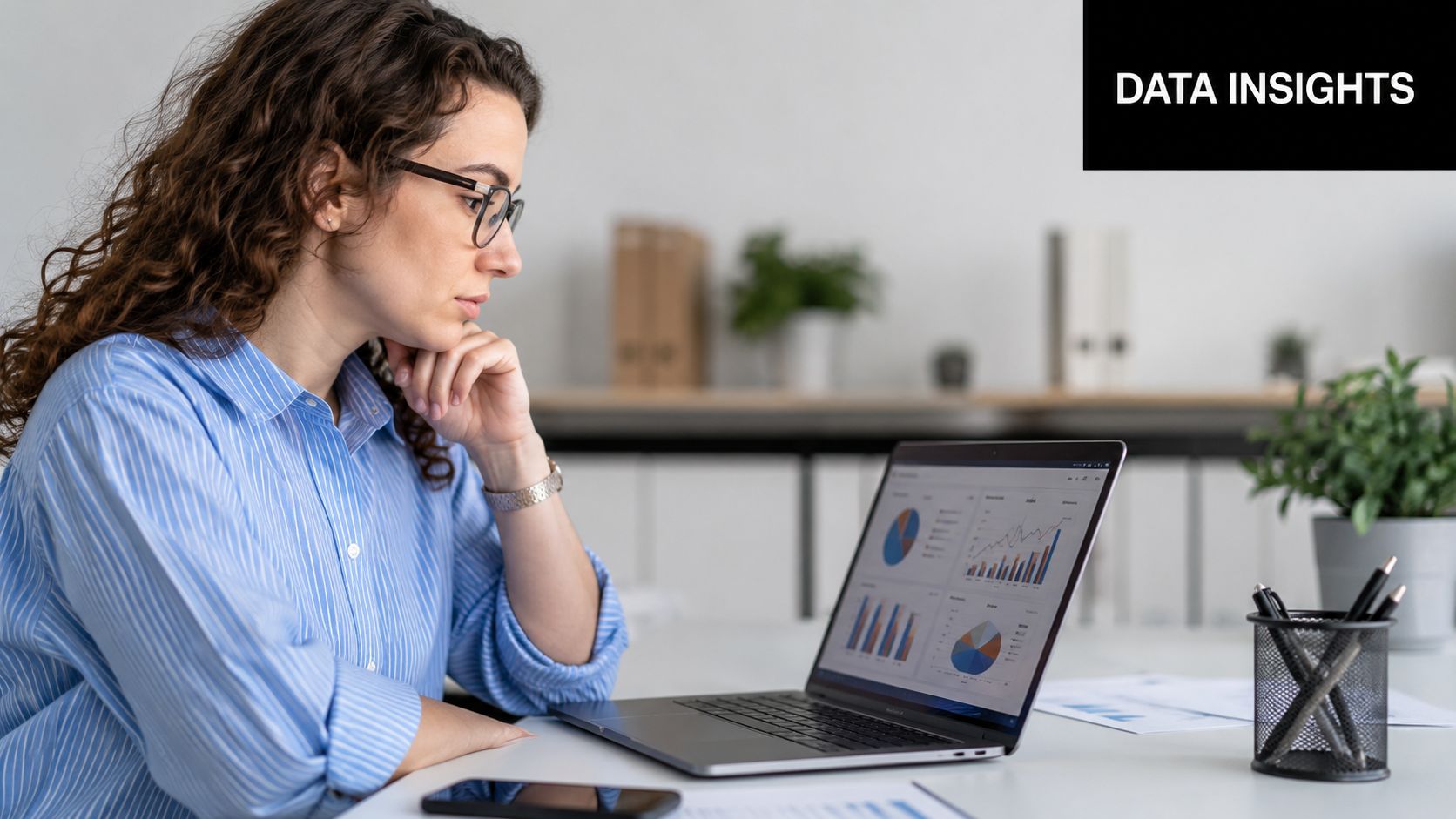 A professional woman in a blue shirt analyzing business data charts on her laptop at her desk.