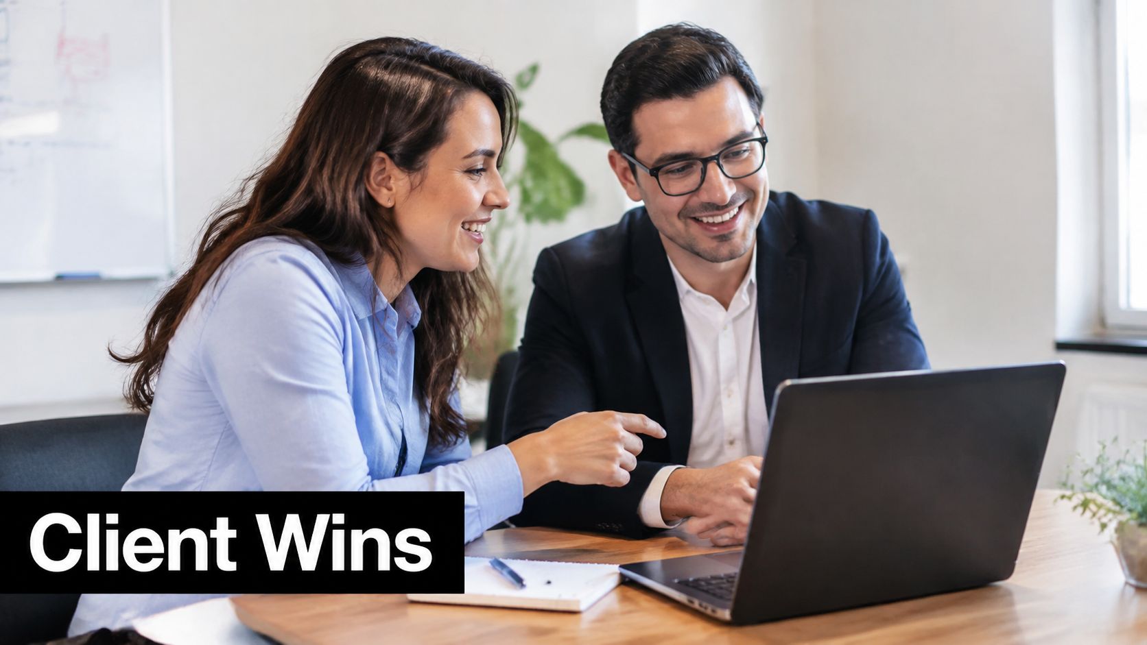 A professional man and woman smiling while looking at a laptop screen during a business meeting.