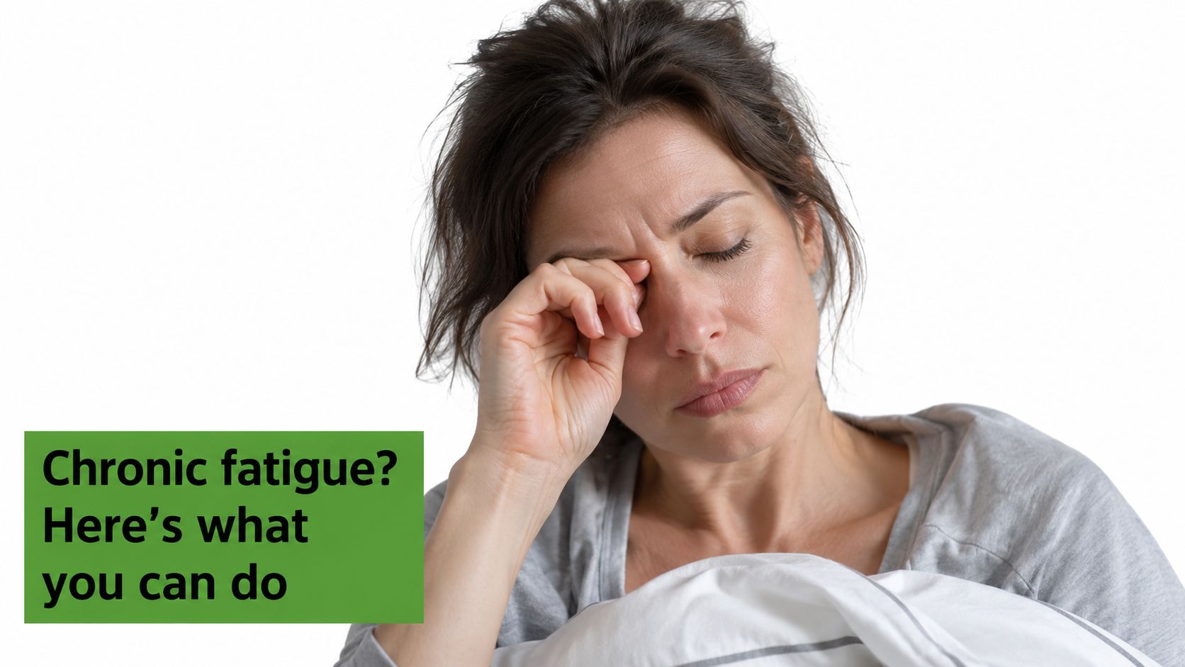 A tired woman rubbing her eye while sitting in bed, representing struggles with chronic fatigue and sleep.