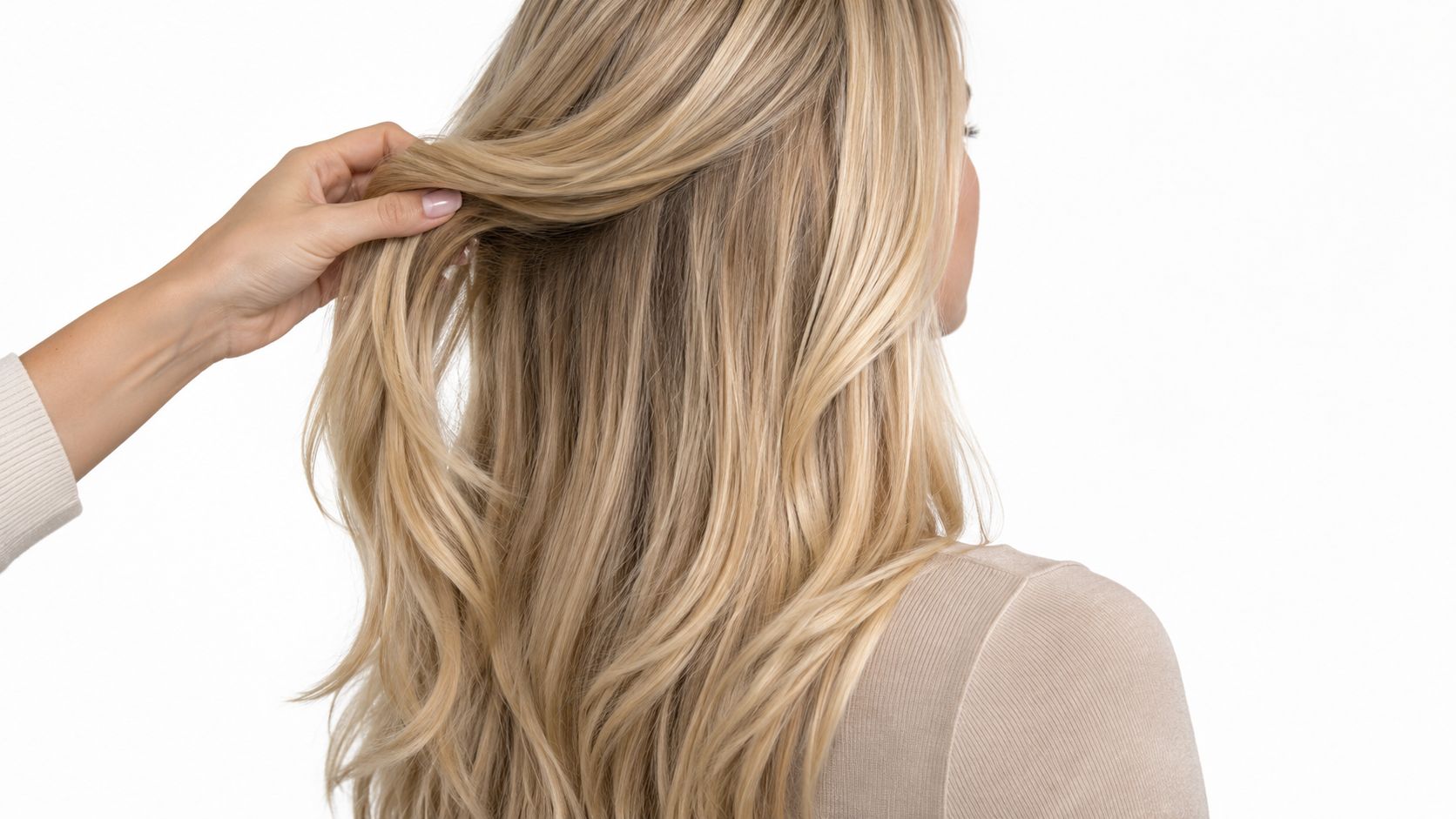 A close-up view of a woman with long blonde hair holding a section of her hair extensions.