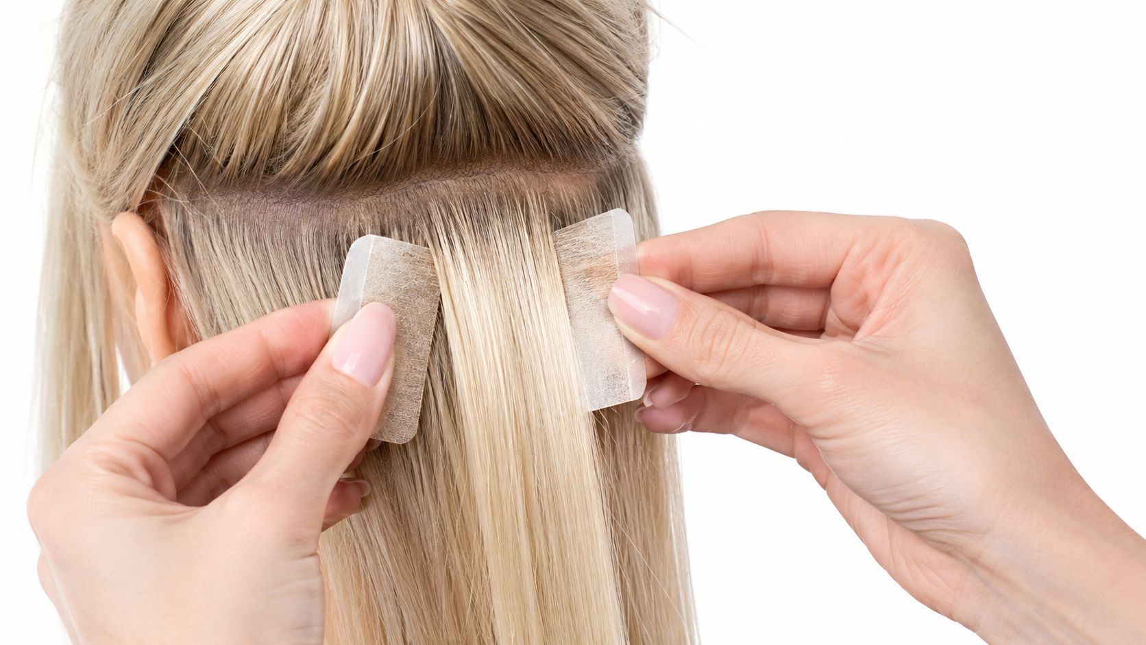 A professional stylist carefully applying tape-in hair extensions to a client with blonde hair.