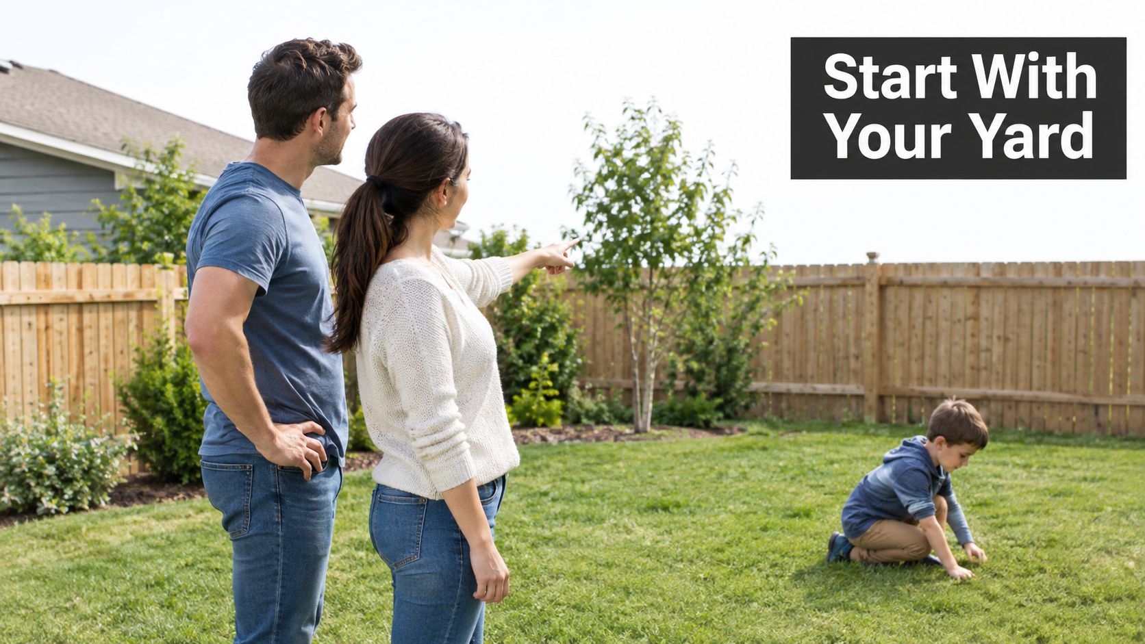 A couple standing in their backyard with a young child playing on the green grass nearby.