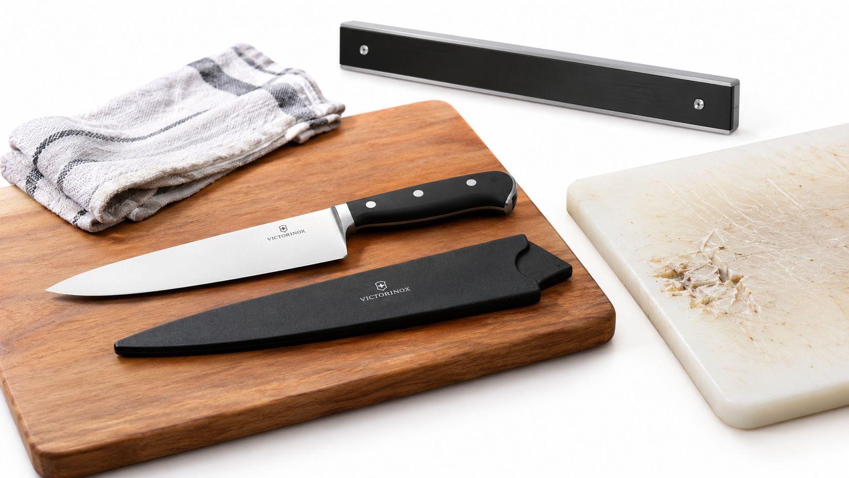 A professional chef knife with a black handle, protective sheath, wooden board, and kitchen items.