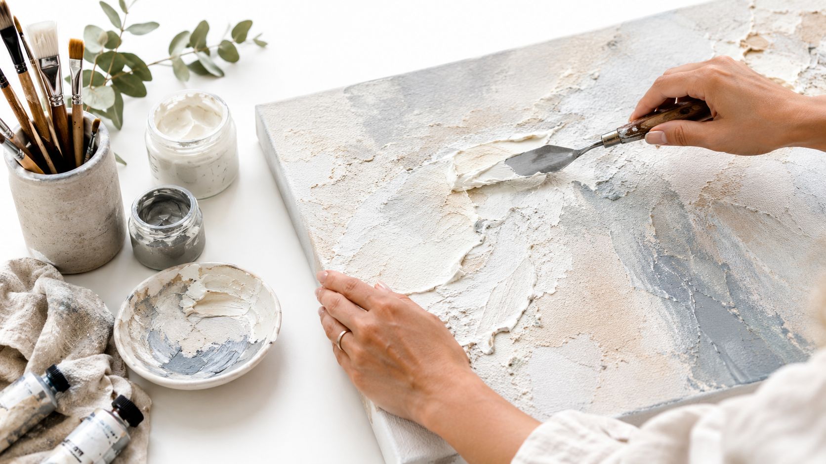 An artist applying white texture paste to a canvas using a metal palette knife for modern painting.