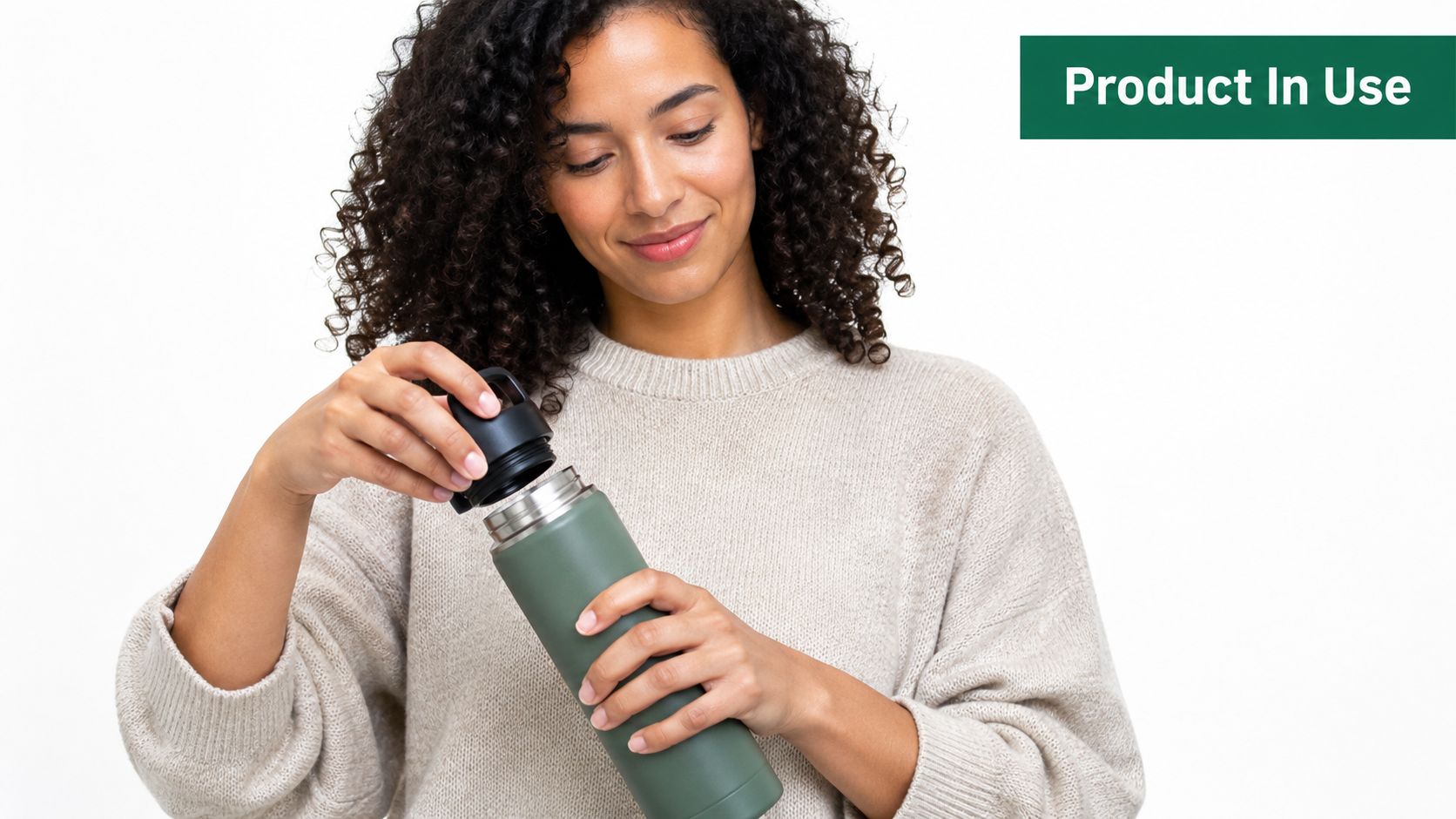 A woman with curly hair smiles while opening a reusable green thermos water bottle in studio