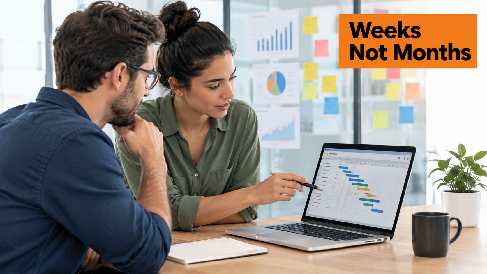A professional man and woman looking at a project timeline on a laptop during an office meeting.