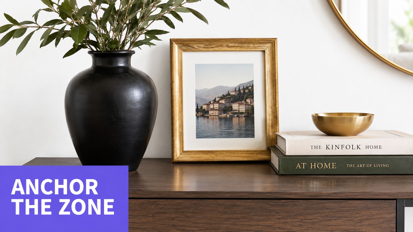 A black vase with branches next to a golden picture frame and stacked books on a table.