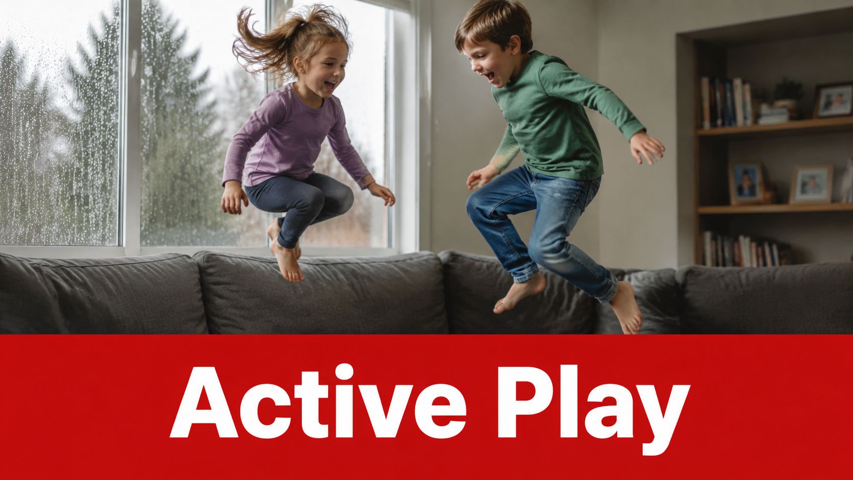 Two happy children jumping playfully together on a gray sofa in a brightly lit indoor living room.
