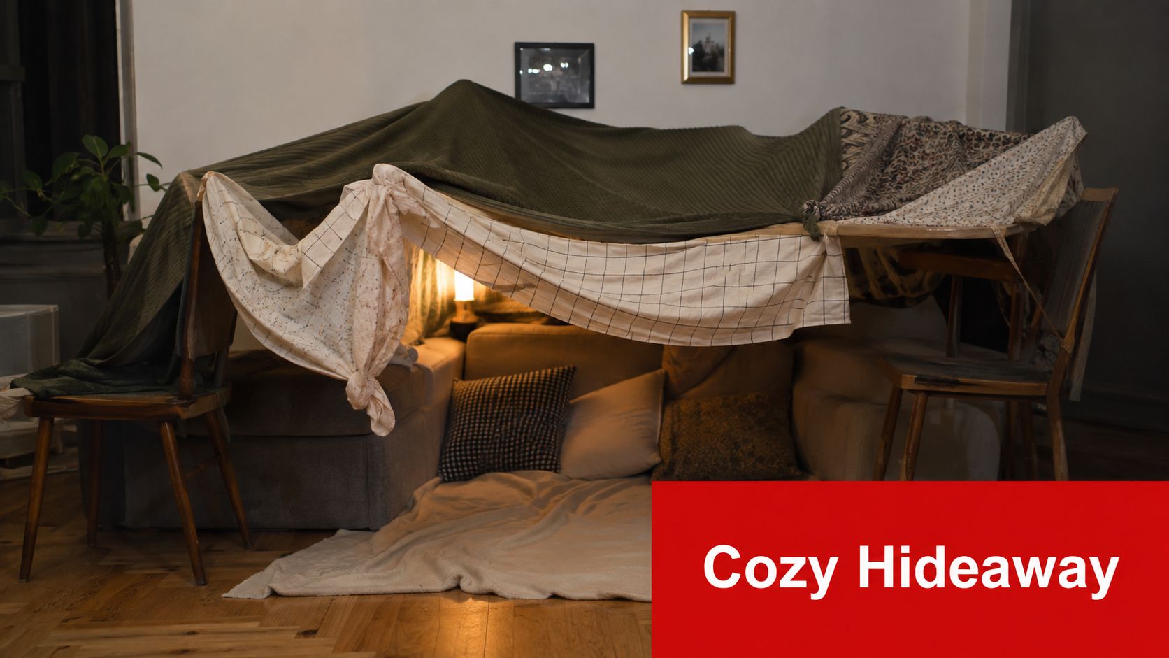 A cozy DIY indoor blanket fort constructed using chairs, sofa cushions, and fabric covers in a living room.