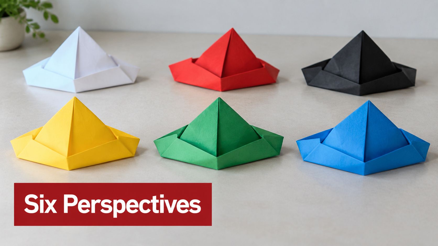 Six colorful origami paper hats arranged in two rows on a light gray table background.