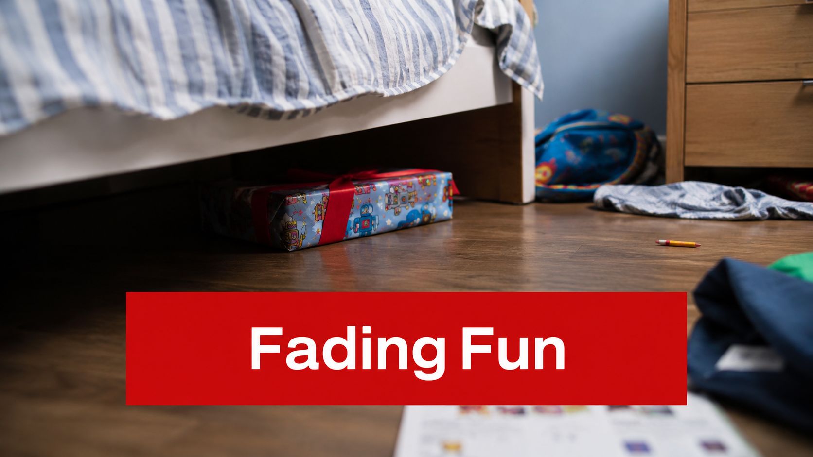 A brightly wrapped gift box hidden under a bed in a child's bedroom with toys scattered around.