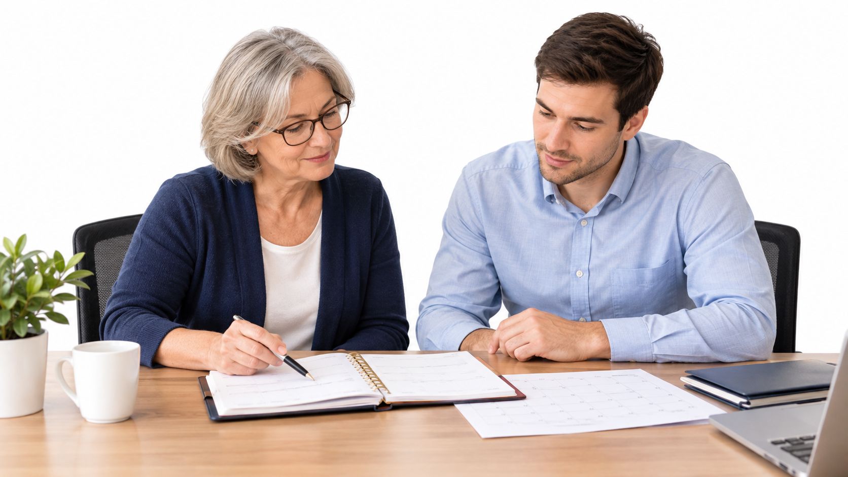 A mature female manager and a younger male colleague reviewing a professional calendar together at a desk.