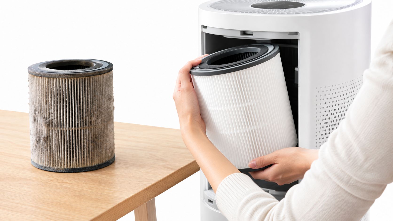 A person replaces a dirty air purifier filter with a clean new one on a wooden table.