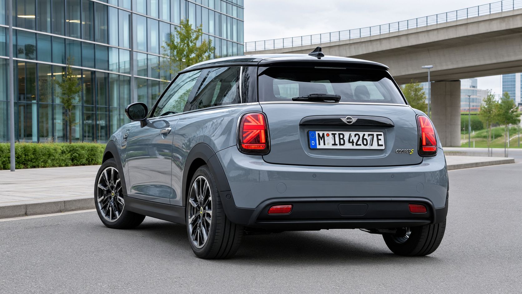 Современный серый Mini Cooper S Electric, припаркованный на городской улице рядом со стеклянным зданием.