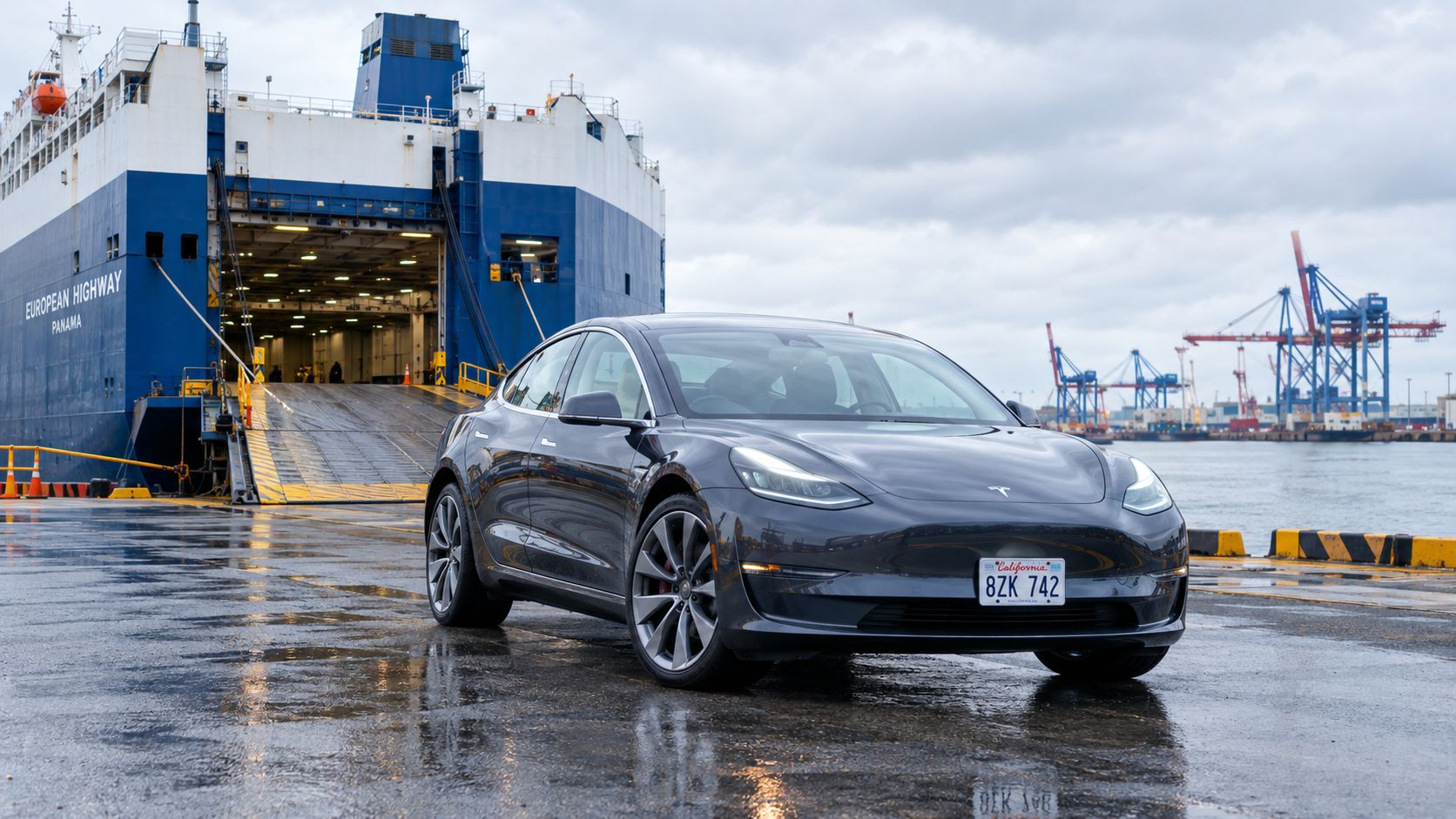 Темно-серый электрический автомобиль Tesla, припаркованный на мокром причале в порту перед большим грузовым судном.