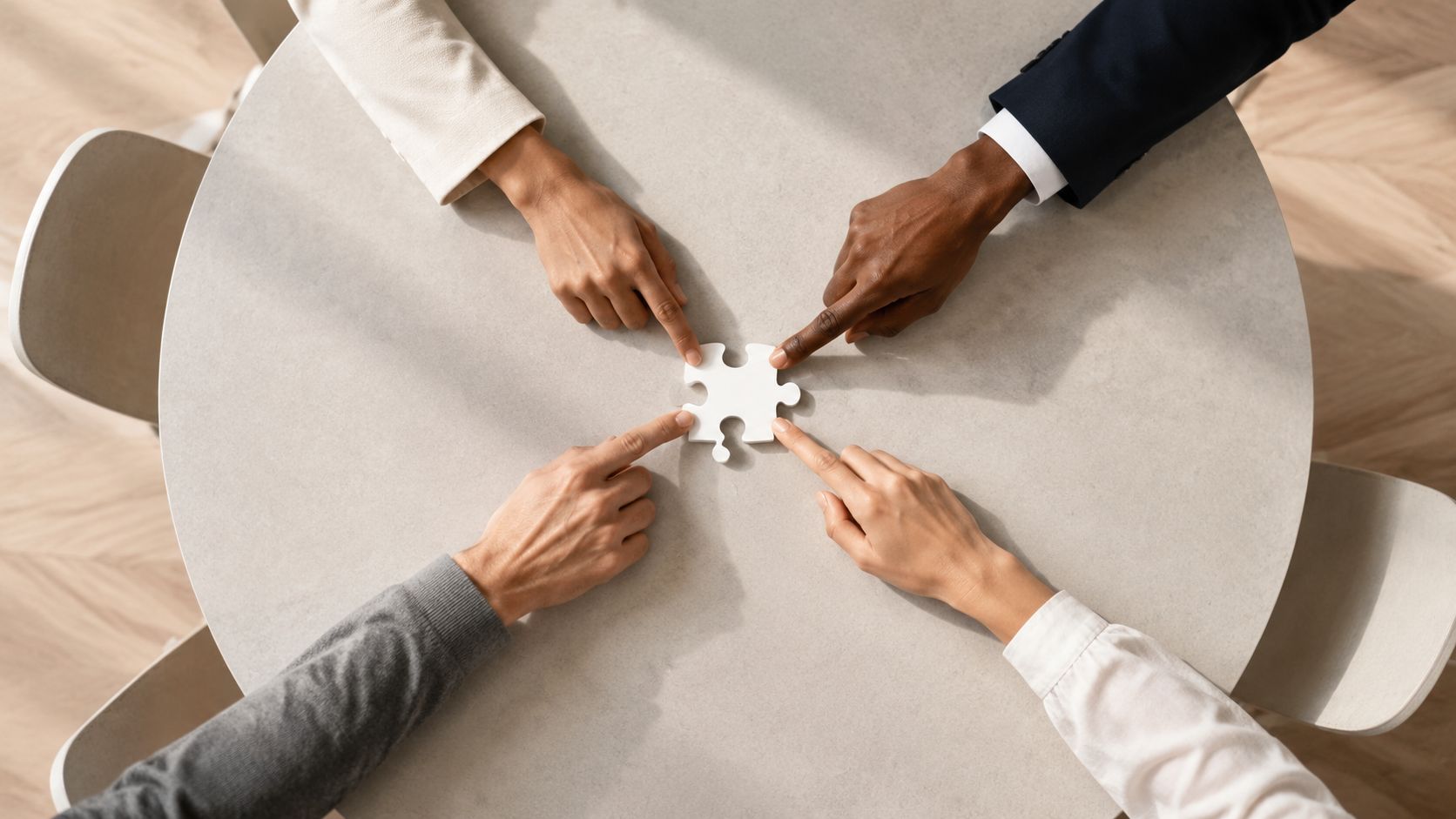 Four business people from diverse backgrounds using their fingers to touch a single white puzzle piece.