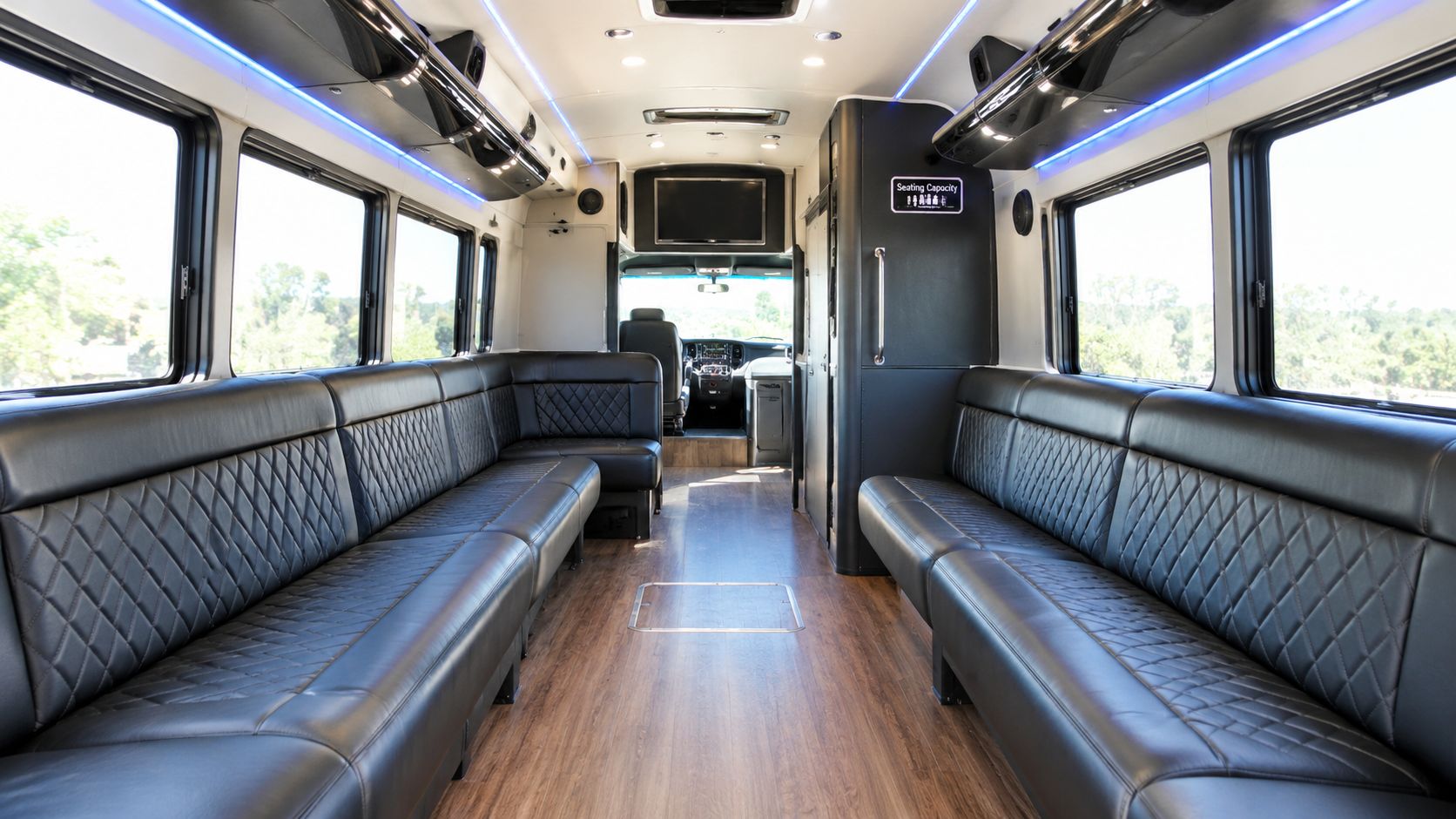 The interior of a luxurious party bus with sleek black diamond-stitched leather bench seating and hardwood floors.