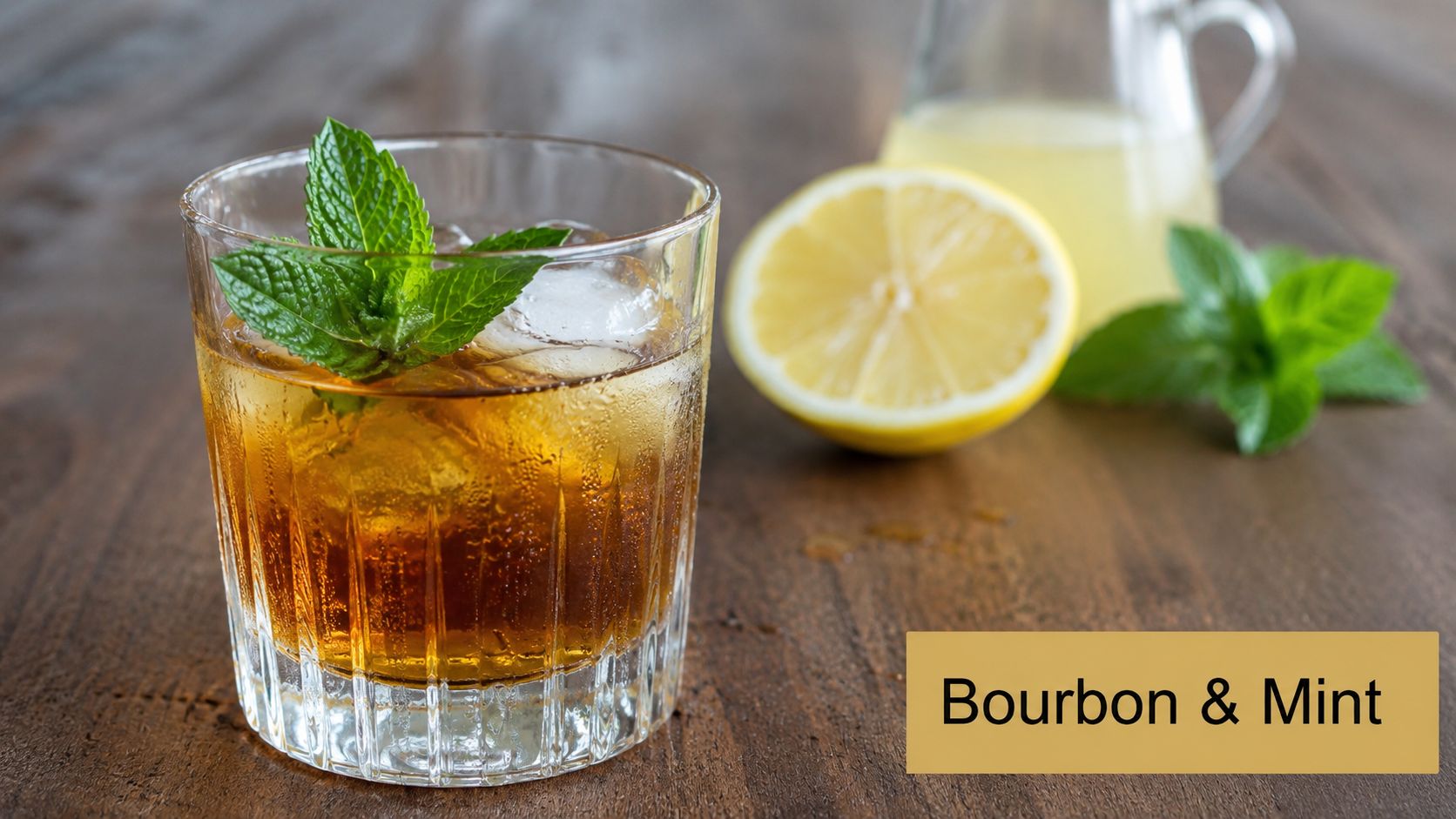 A glass of bourbon and mint cocktail placed on a wooden table next to fresh lemons.