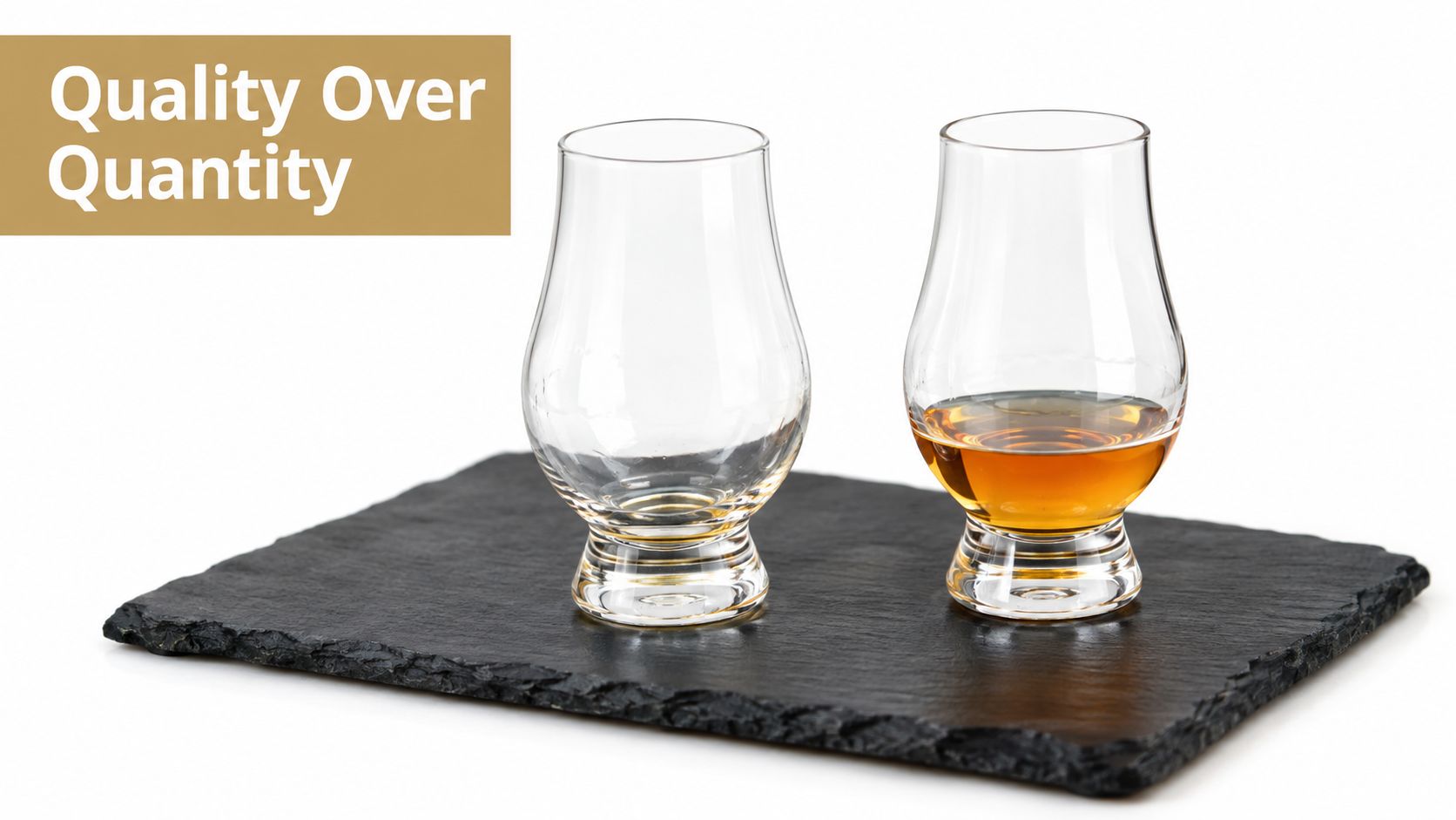 Two Glencairn glasses sitting on a slate board, one empty and one containing a splash of whisky.