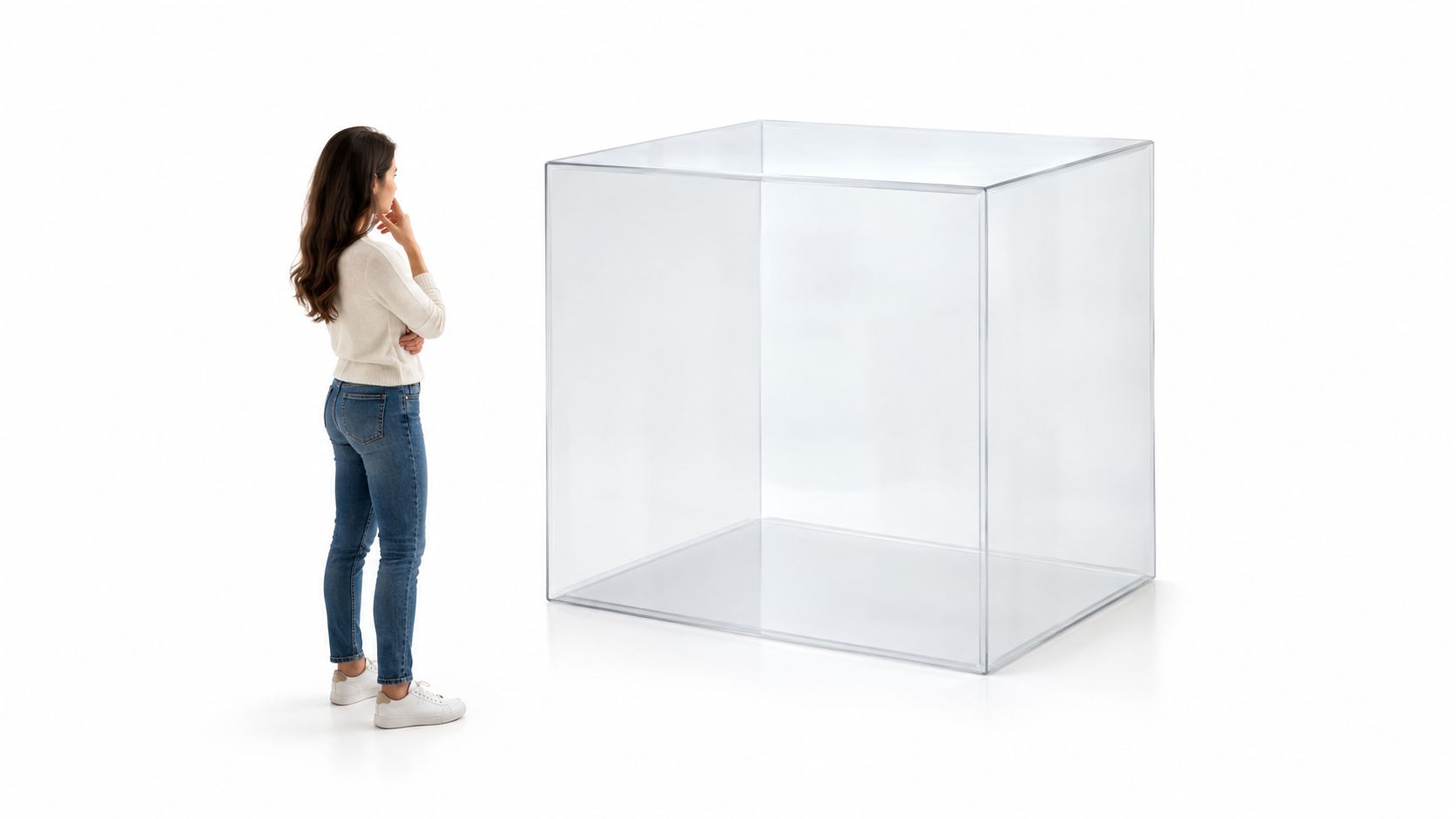 A woman stands thoughtfully looking at a large, empty transparent glass cube against a white background.