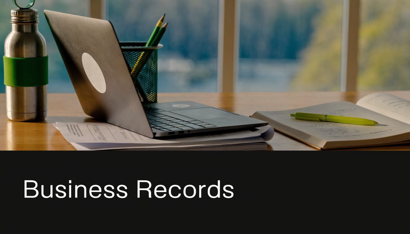 A modern desk workspace featuring a laptop, notebook, pen, and water bottle for business record keeping.