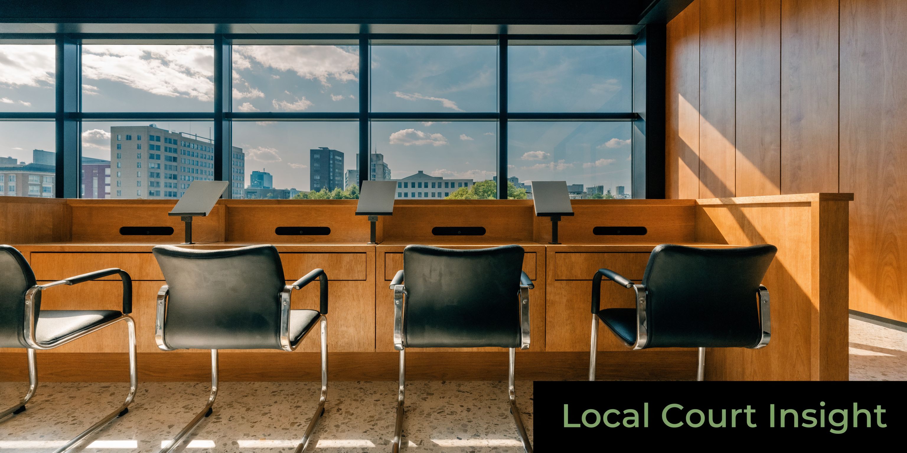 A minimalist courtroom interior with empty chairs facing a large window overlooking a city skyline.