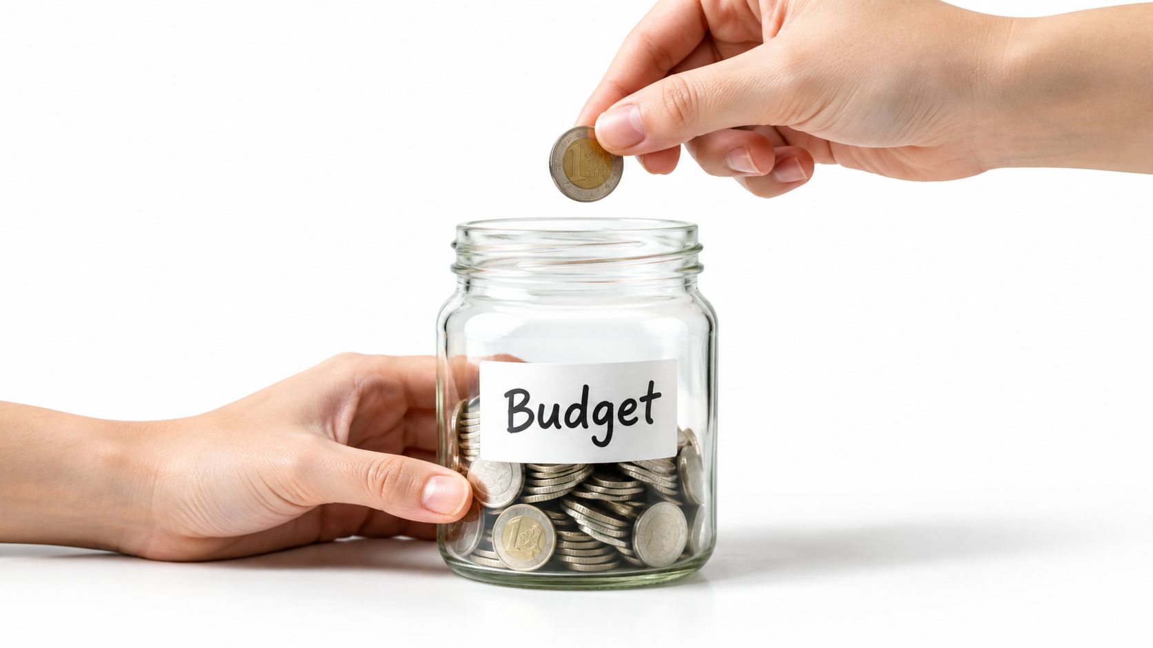 A hand placing a euro coin into a glass jar labeled with the word Budget.
