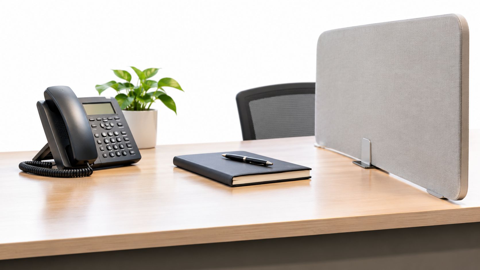 A professional office desk featuring a telephone, notebook, and privacy screen for a corporate environment.