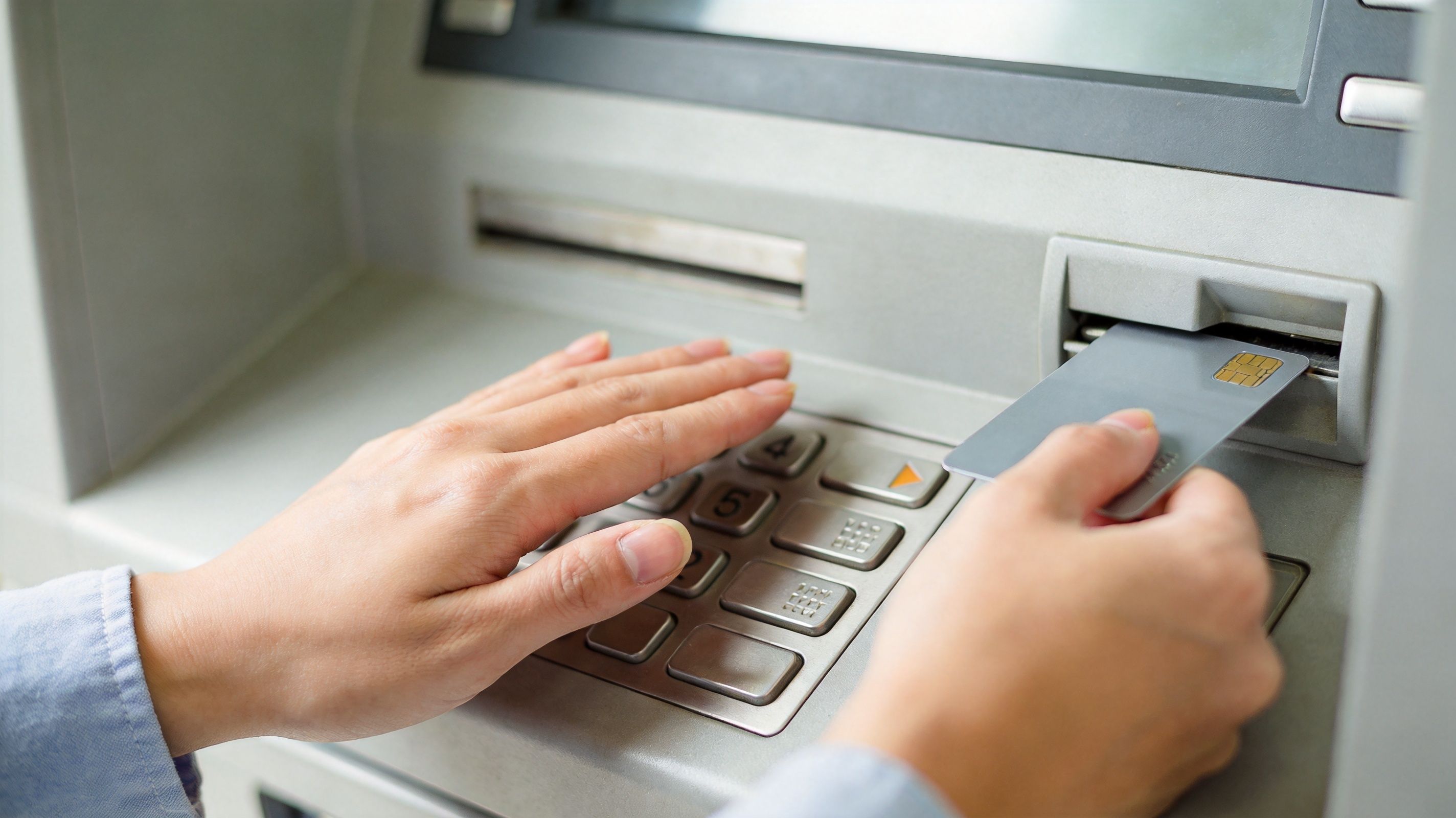 A person uses a credit card to conduct a financial transaction at an outdoor bank ATM.