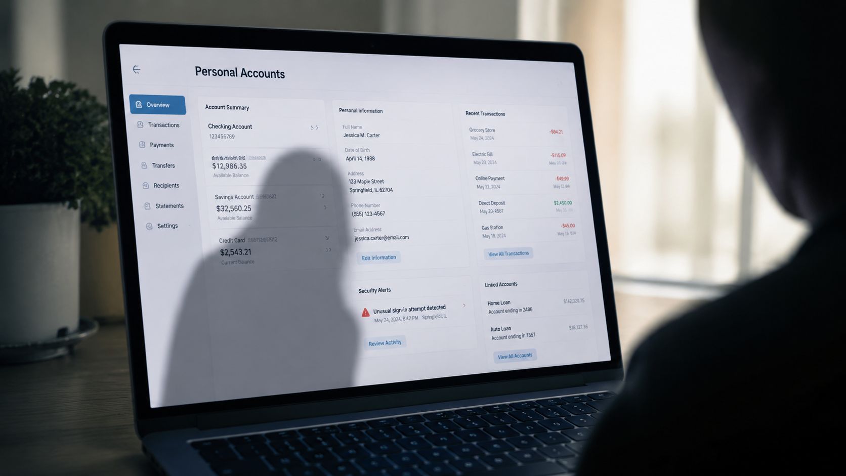 A person using a laptop with a dark silhouette of someone watching their personal financial bank account screen.