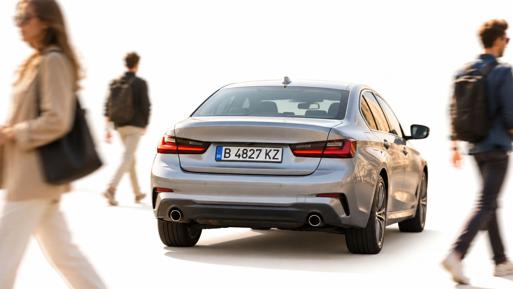 A silver BMW sedan driving on a bright street with blurred pedestrians walking in the background.