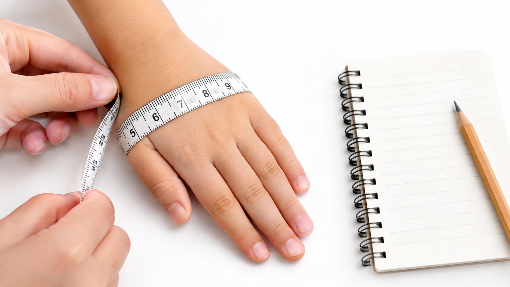 A person measuring a child's wrist with a tape measure next to a notepad and pencil.