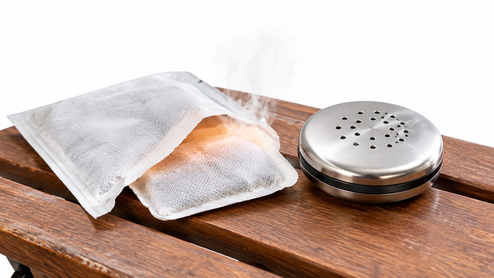 A hand warmer pouch glowing with heat and steam next to a metallic hand warmer on wood.